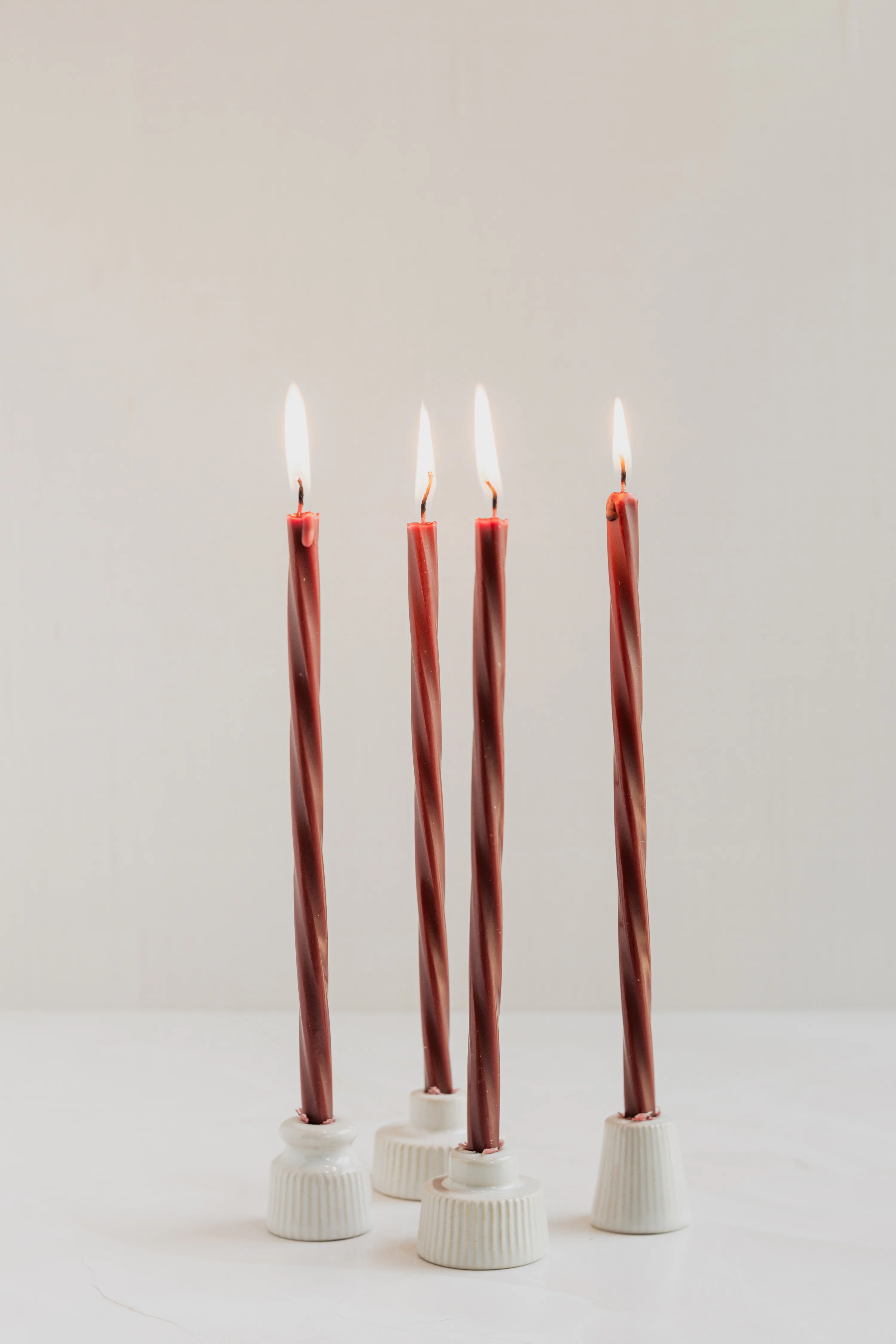 Four lit twisted dark red candles in small white ribbed ceramic holders