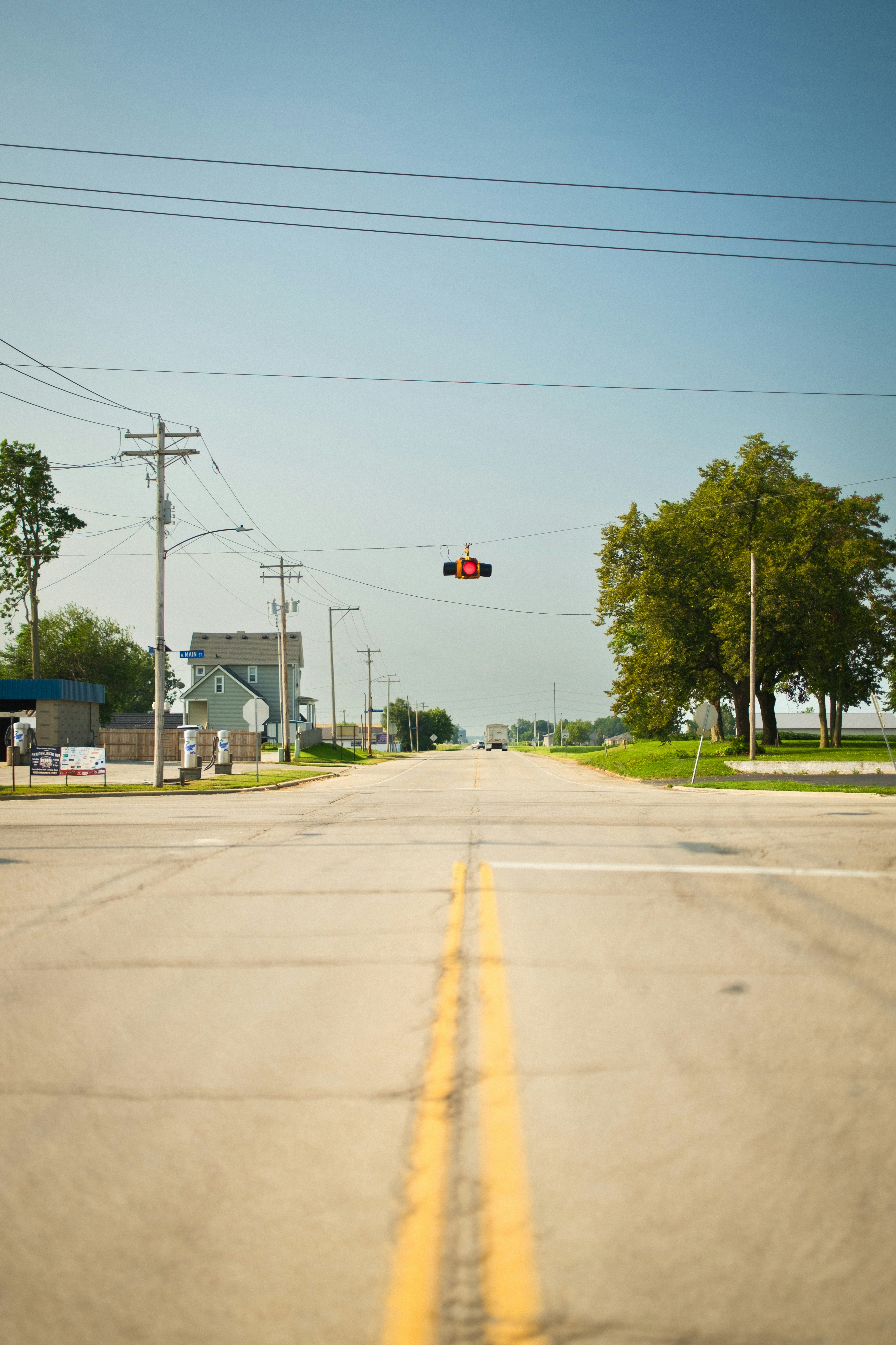 A red traffic light hanging over a quiet road in a small town