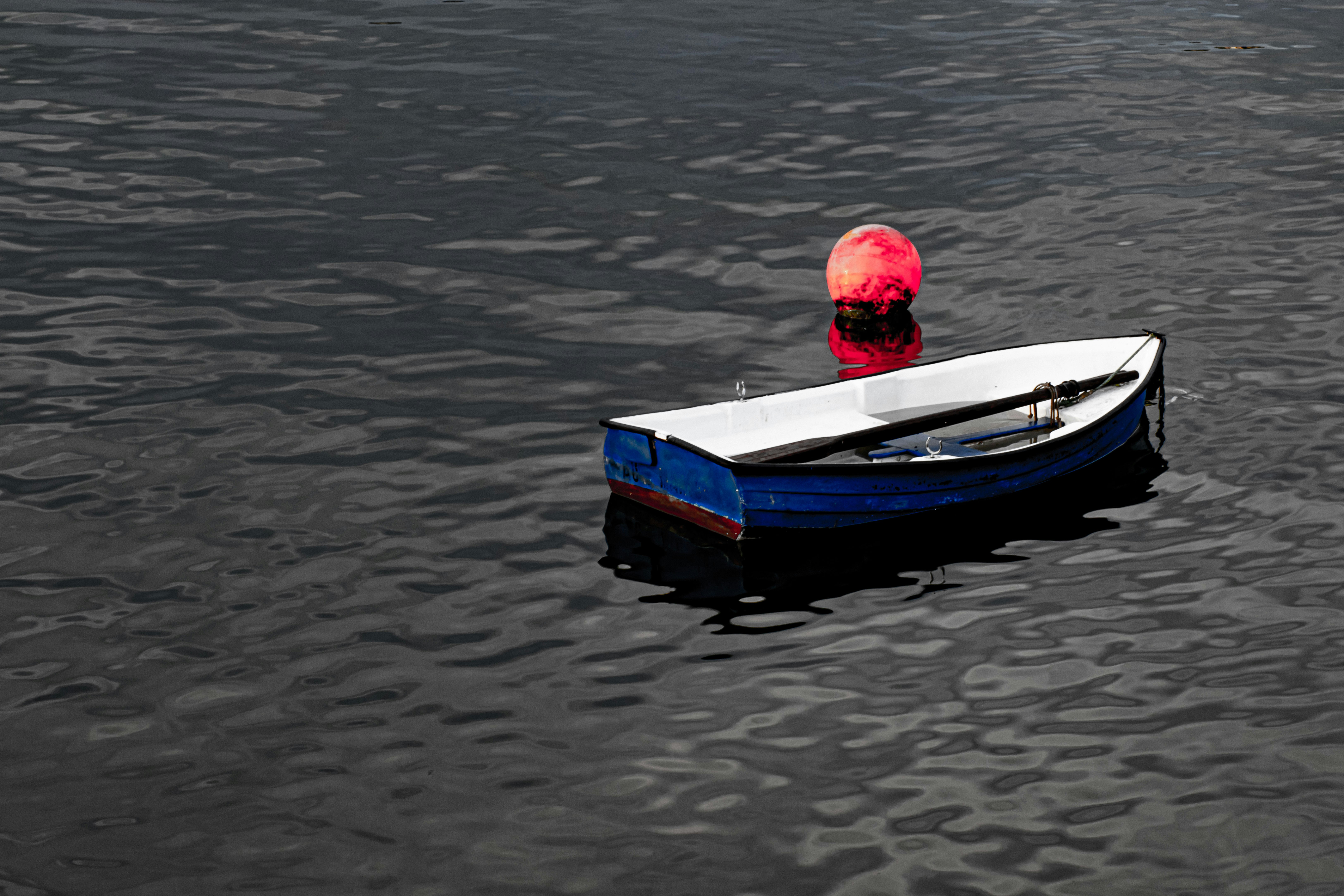 A small blue and white rowboat floating near a red buoy on dark water