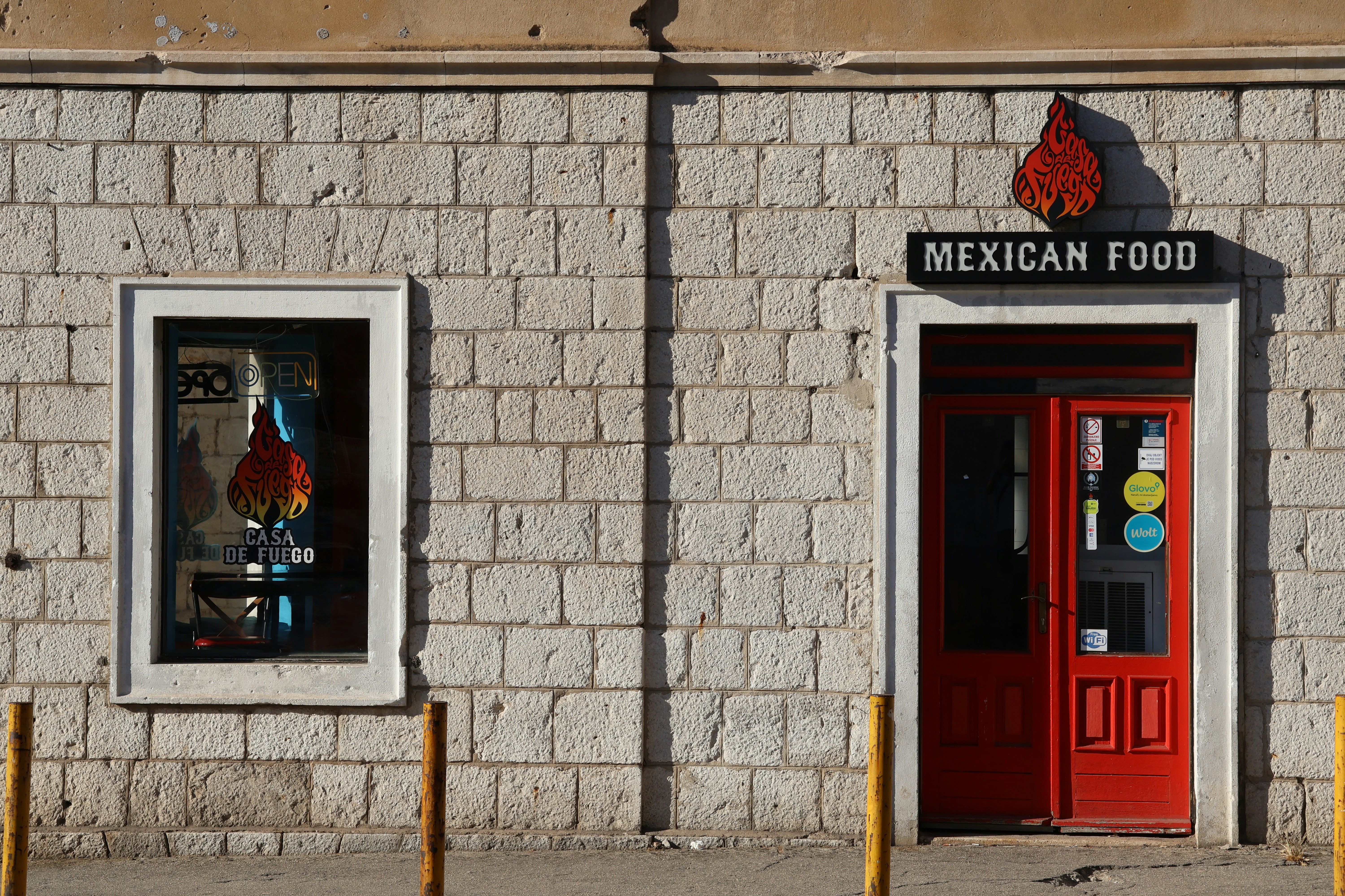 A red door and a window on a stone wall of a Mexican food restaurant