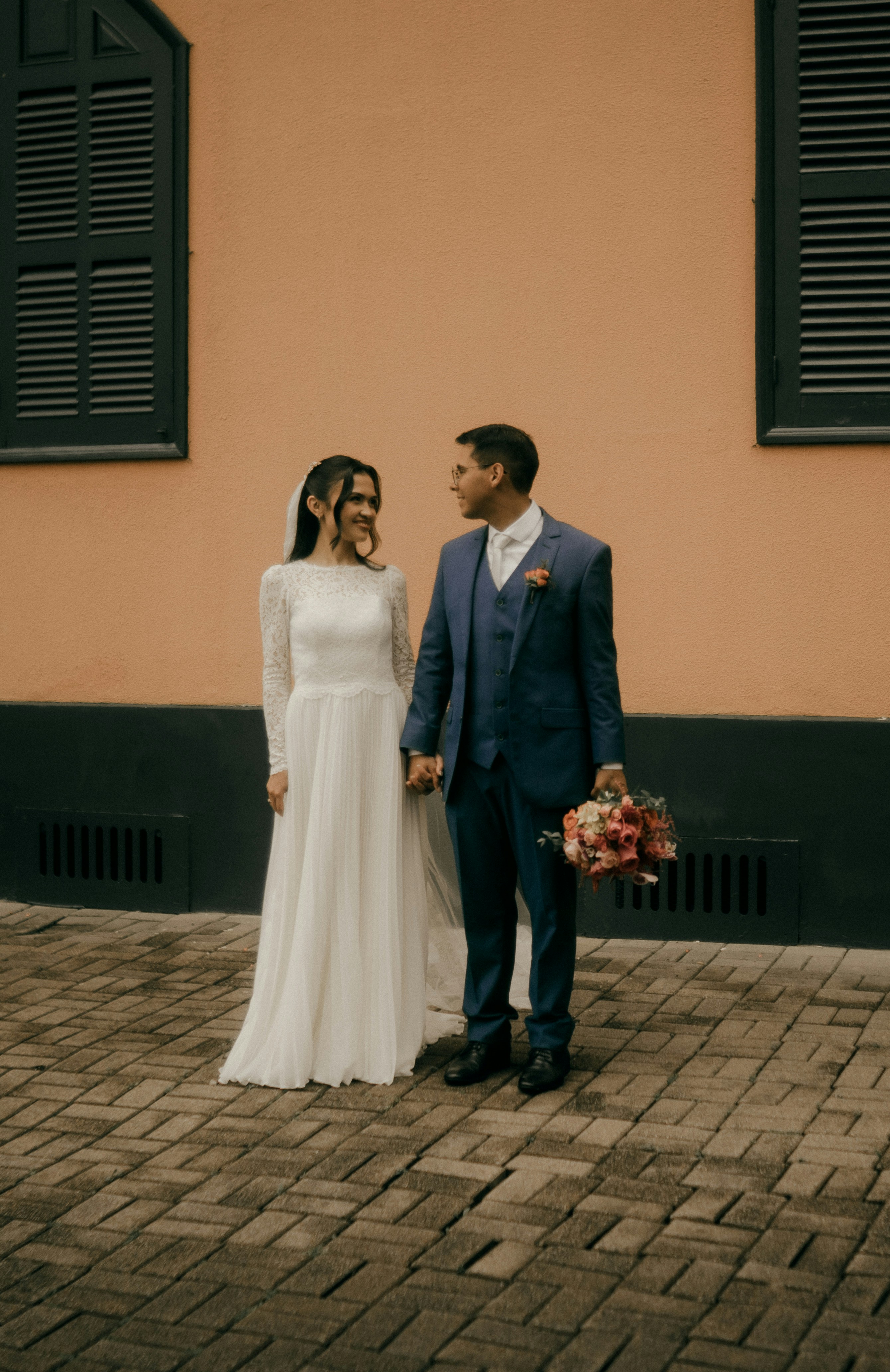 Une mariée et un marié se tenant la main sur un chemin pavé devant un mur de pêche