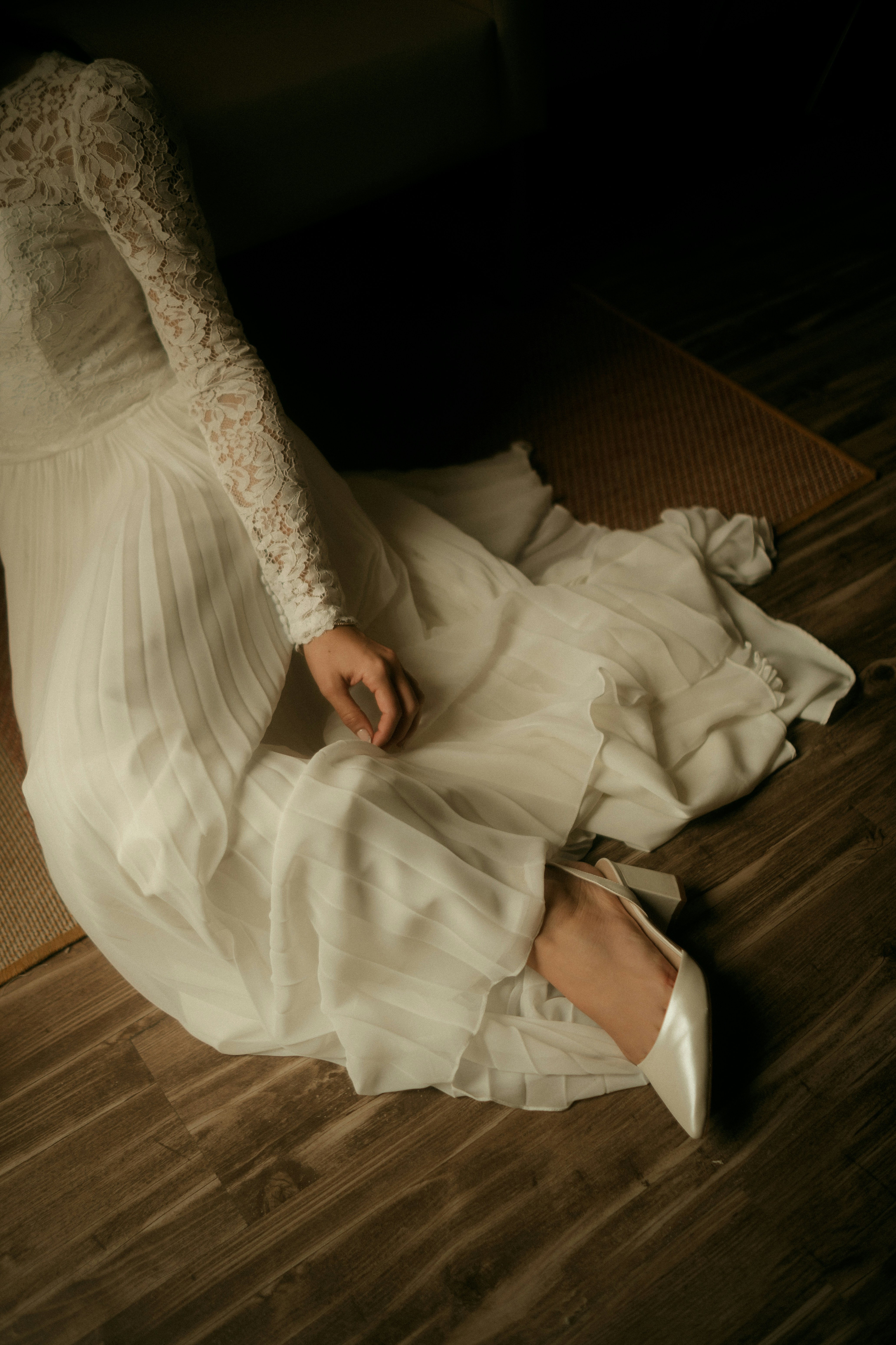 A person in a white lace wedding dress sitting on a wooden floor