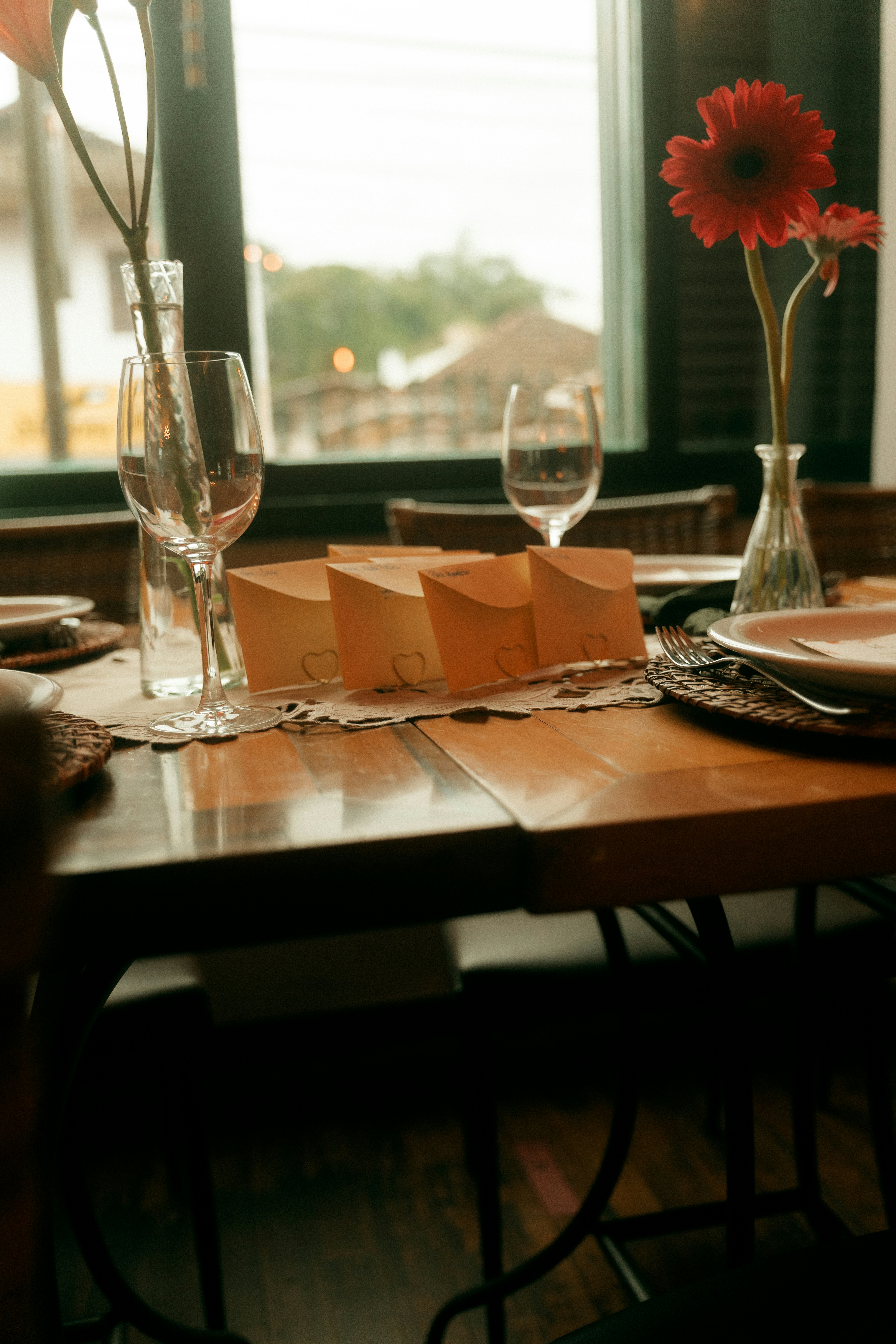 De petites enveloppes avec des pinces en forme de cœur posées sur une table en bois avec des verres à vin et des fleurs