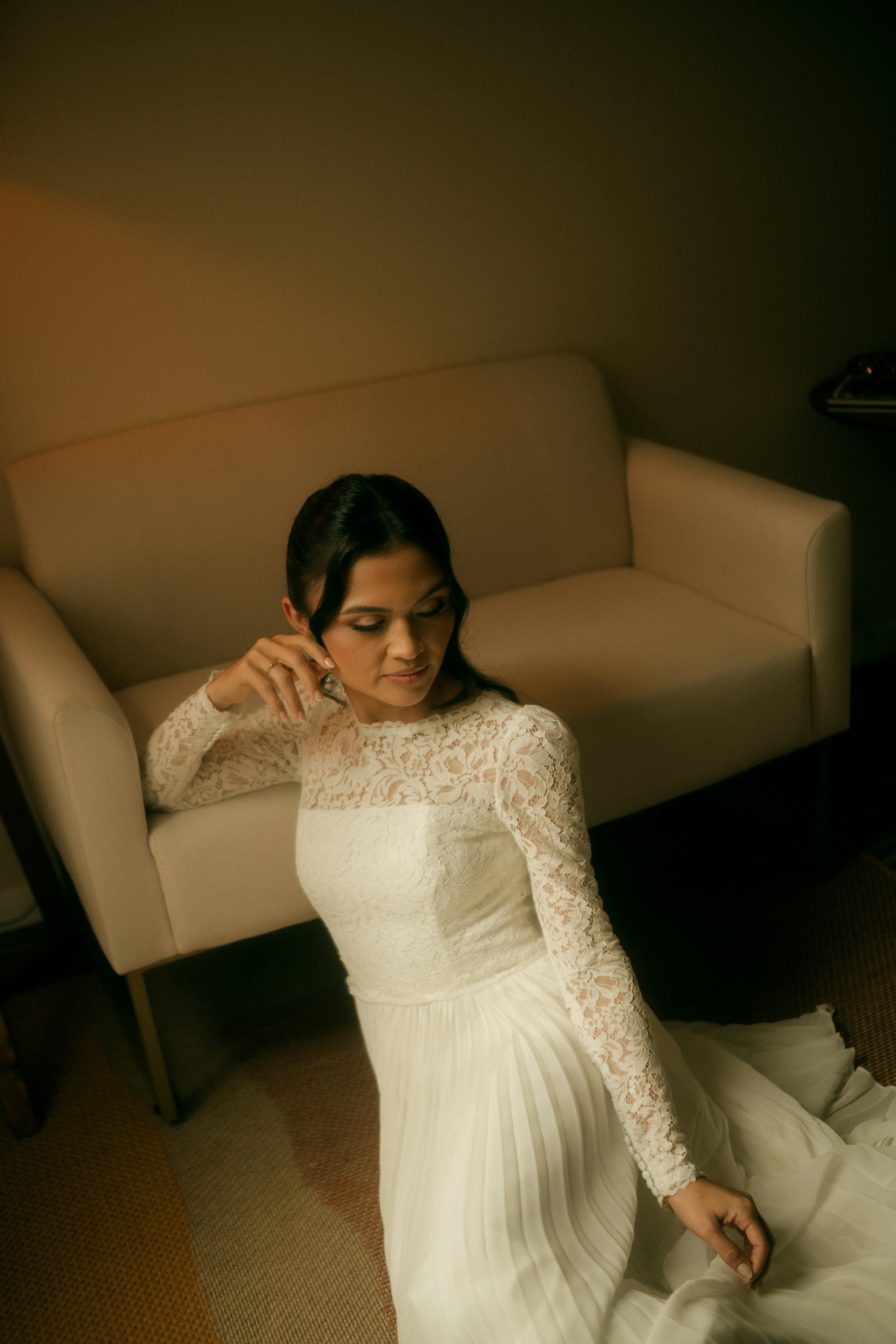 Une femme en robe blanche en dentelle, posée par terre près d’un canapé