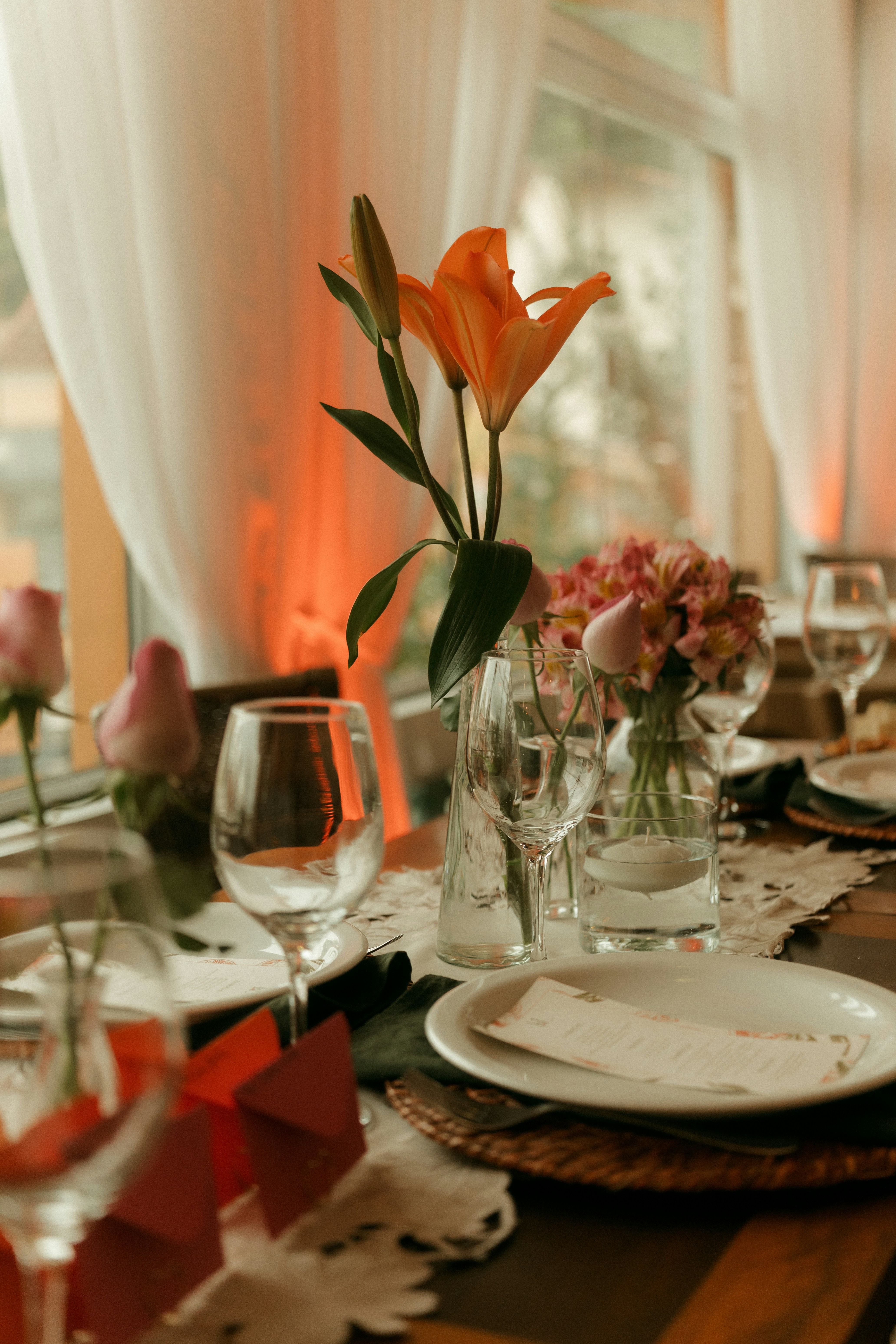 Des lys orange et des fleurs roses dans des vases en verre sur une table à manger décorée