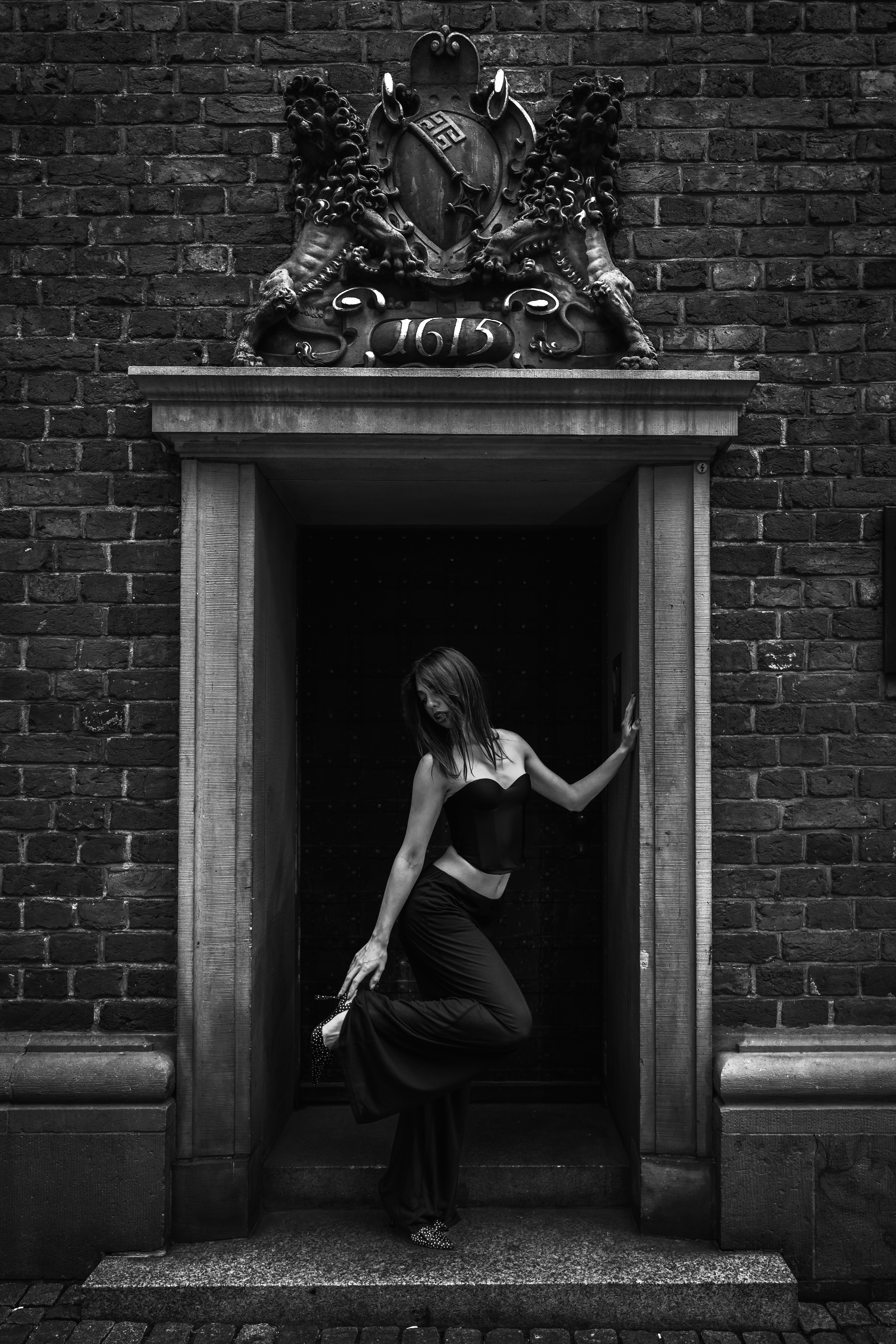 A woman in a black corset and trousers posing in a stone doorway