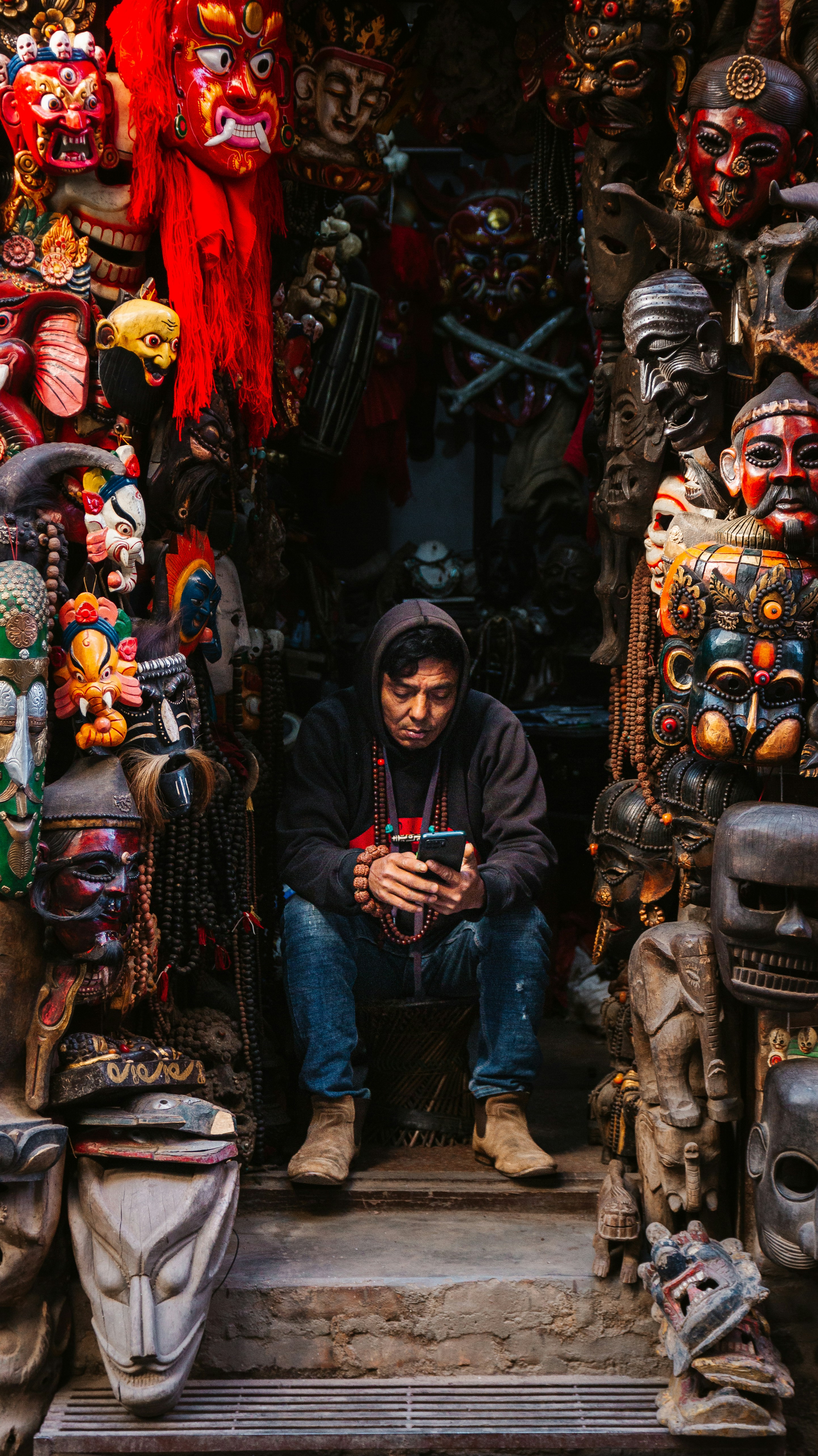 A person in a hoodie using a smartphone surrounded by traditional carved masks