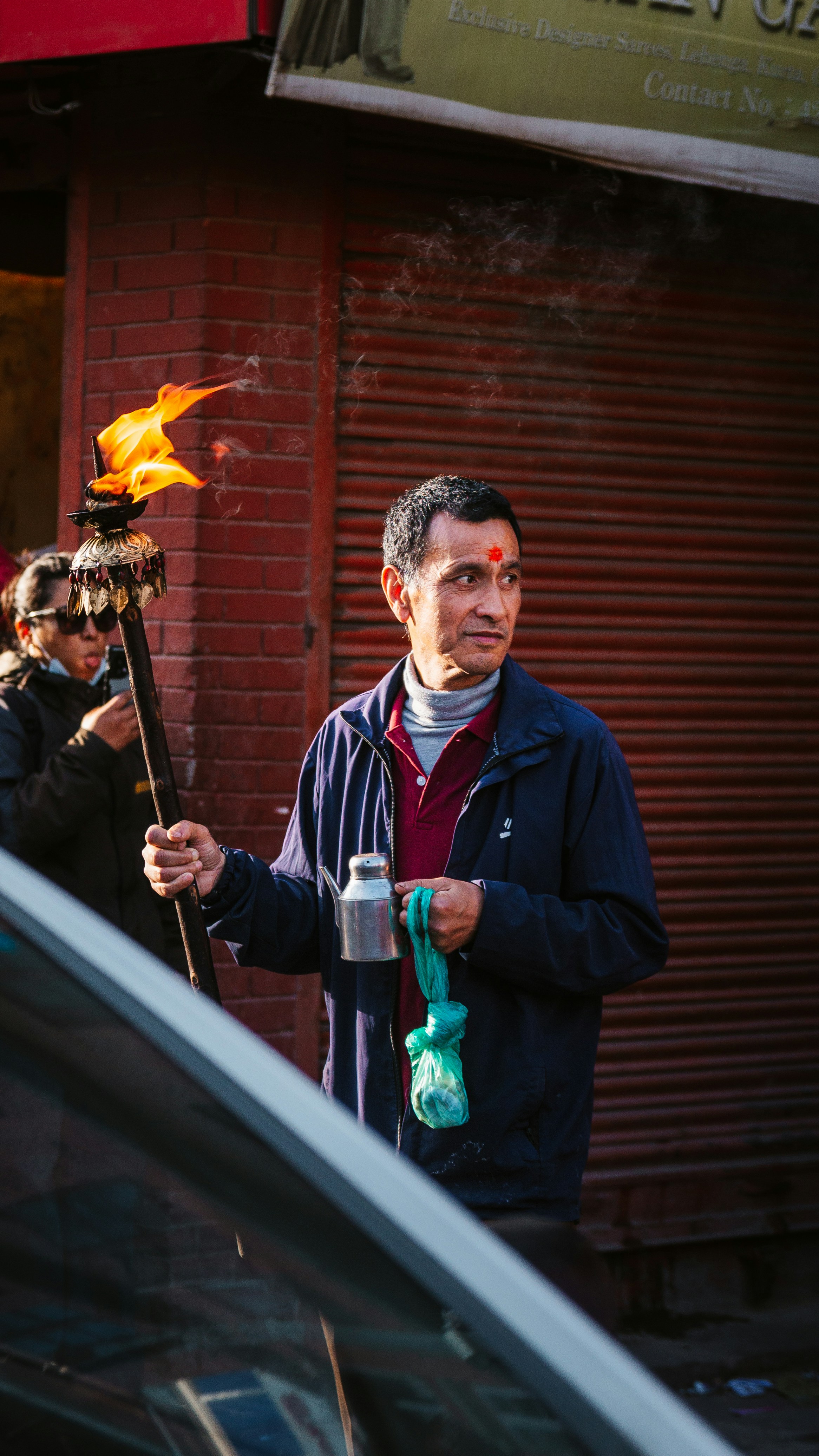 A man holding a flaming torch and a metal pot on a city street