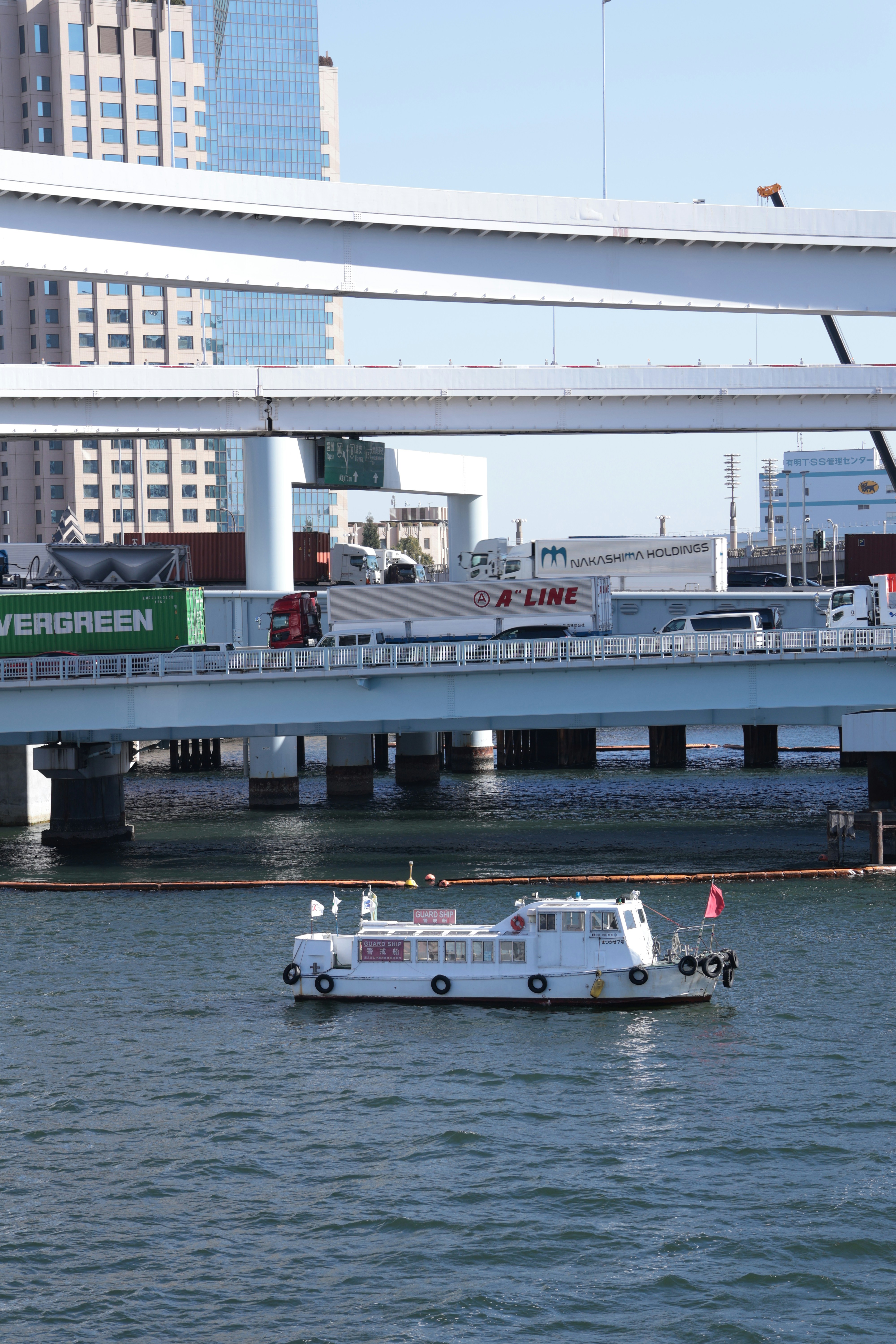 多層の高速道路橋の下の水面に浮かぶ白い警備船