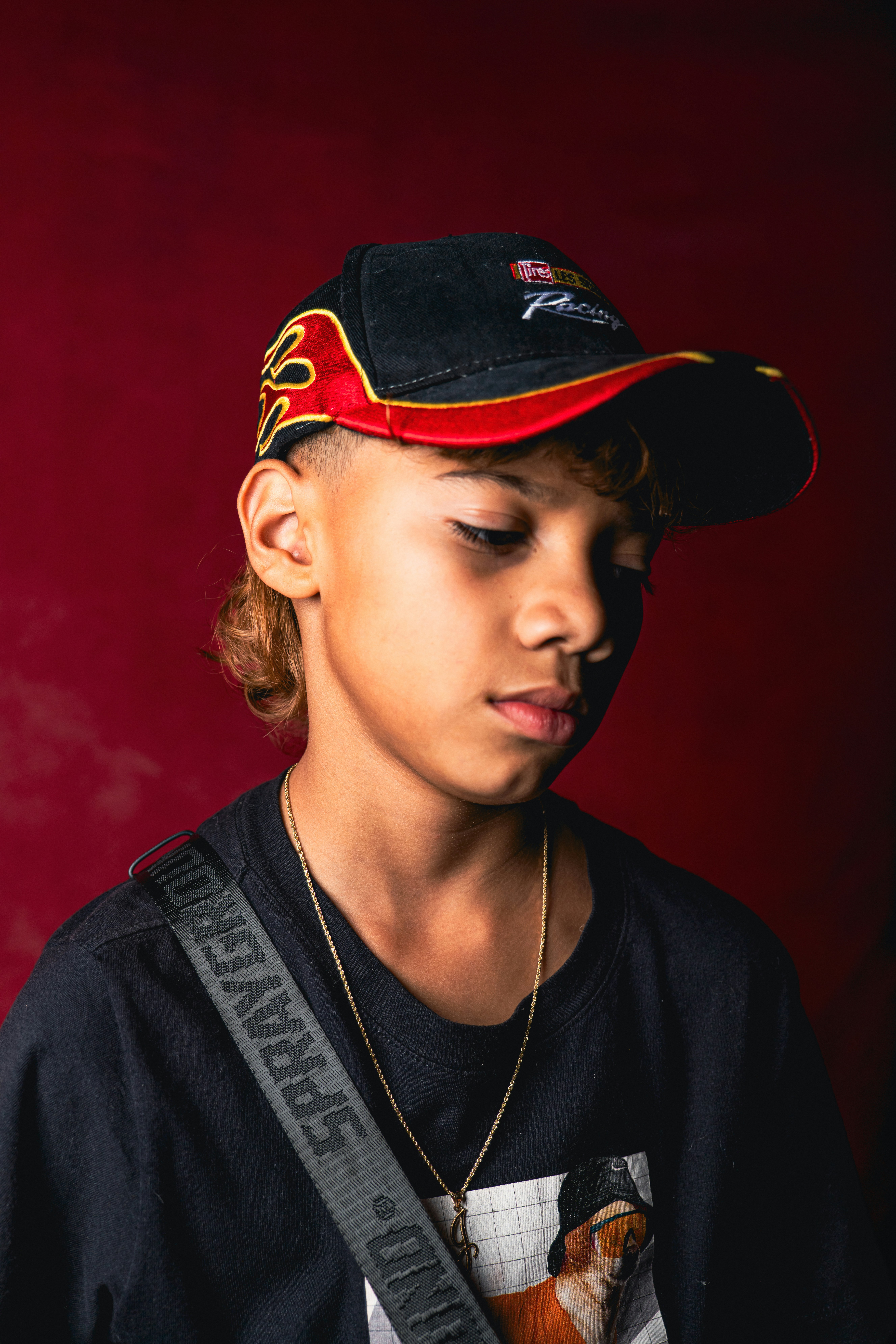 A person wearing a black racing cap and t-shirt against a dark red background