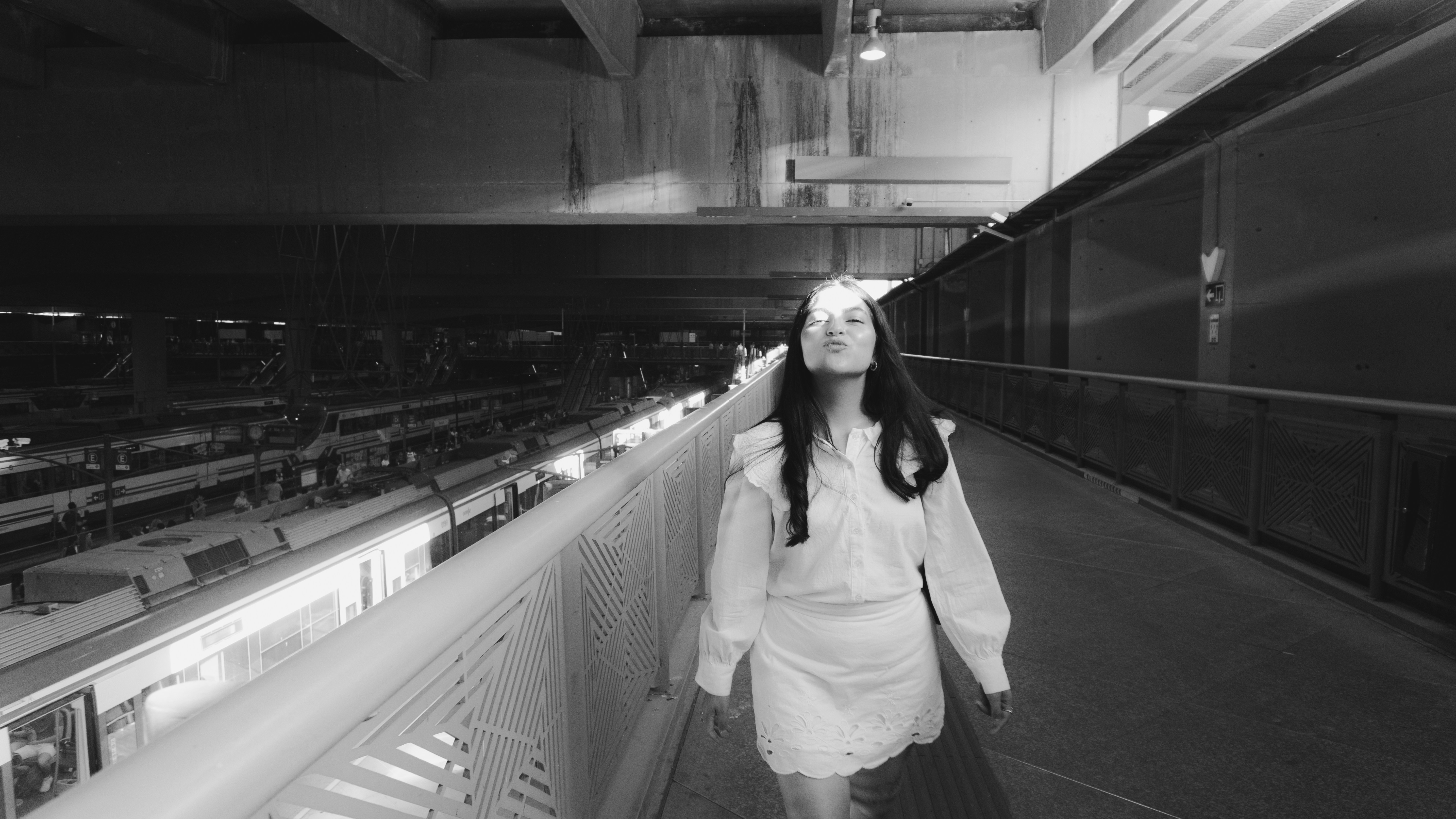 A woman in a white blouse and skirt walking on a train station walkway