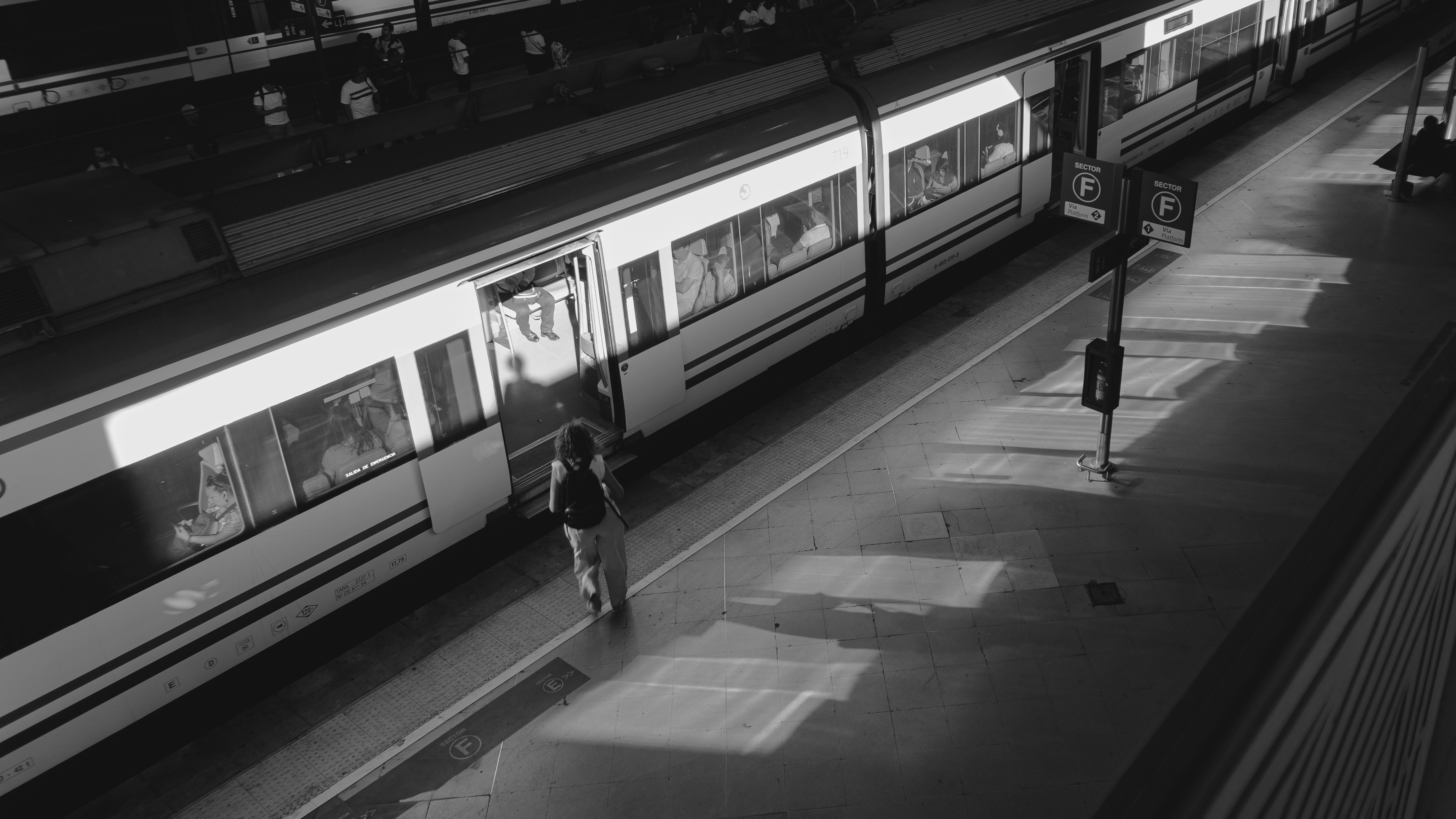 A person with a backpack boarding a train at a platform in black and white