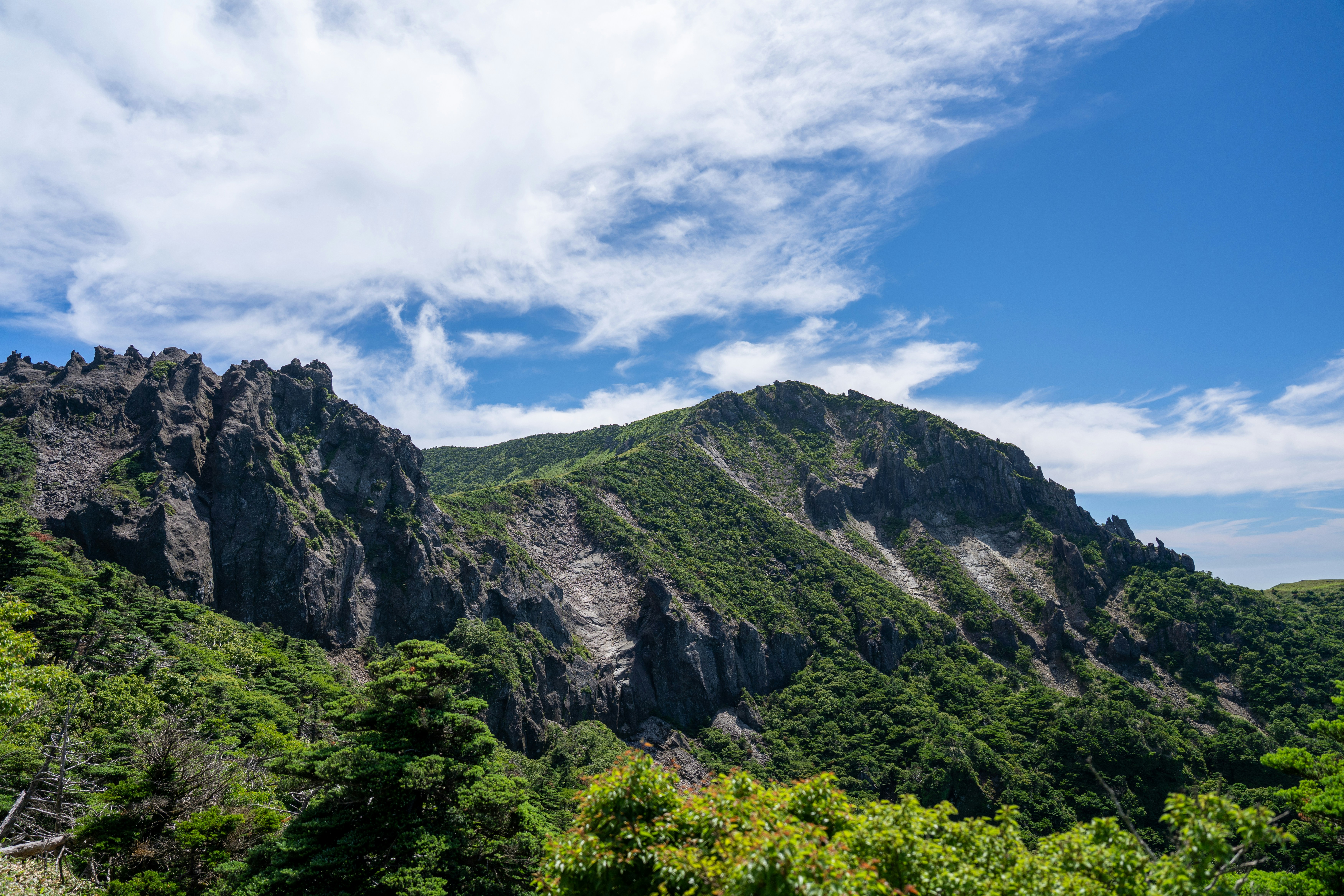 Rugged rocky mountain peaks covered in green vegetation under a bright blue sky