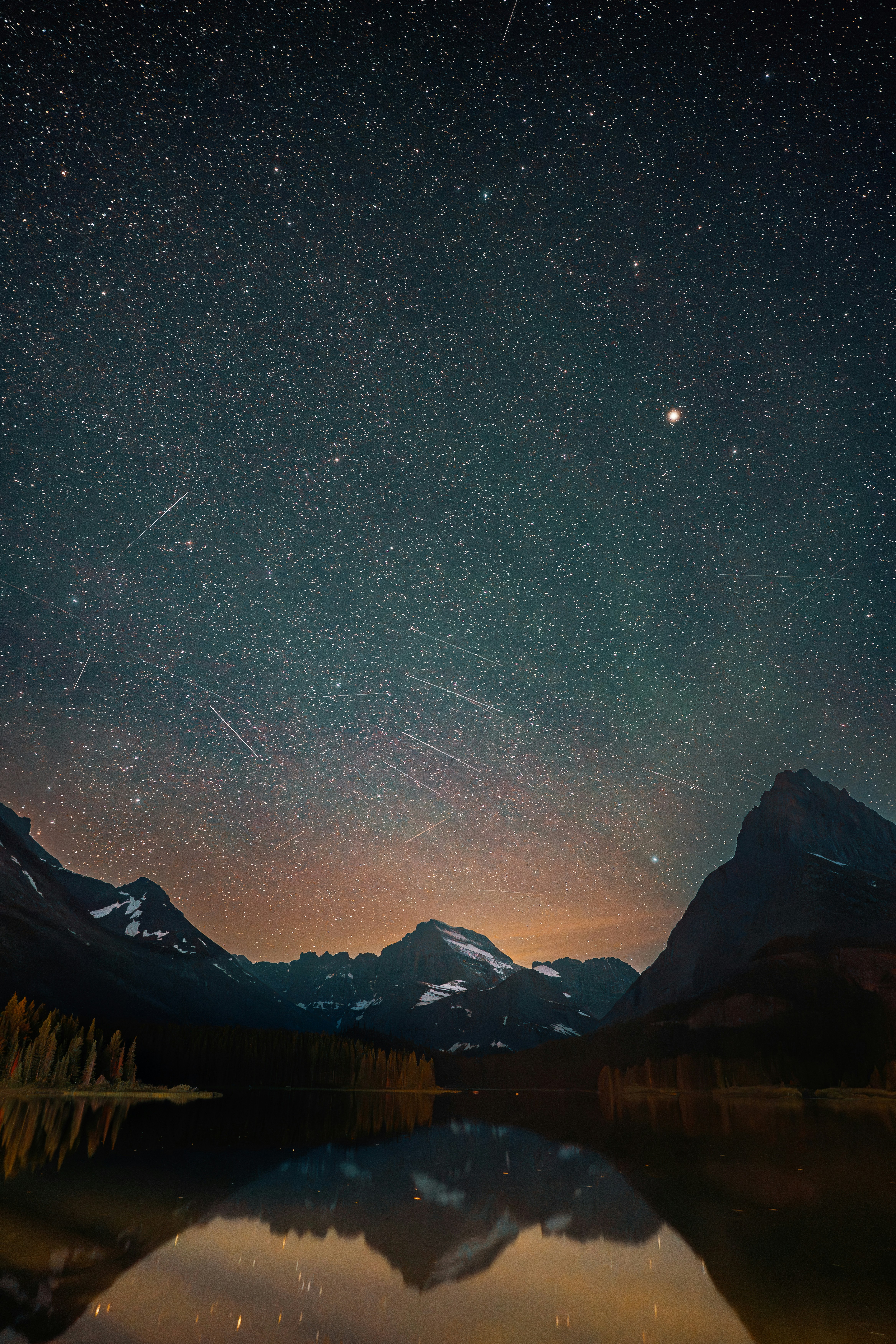 A starry night sky with meteor streaks above dark mountains and a reflective lake