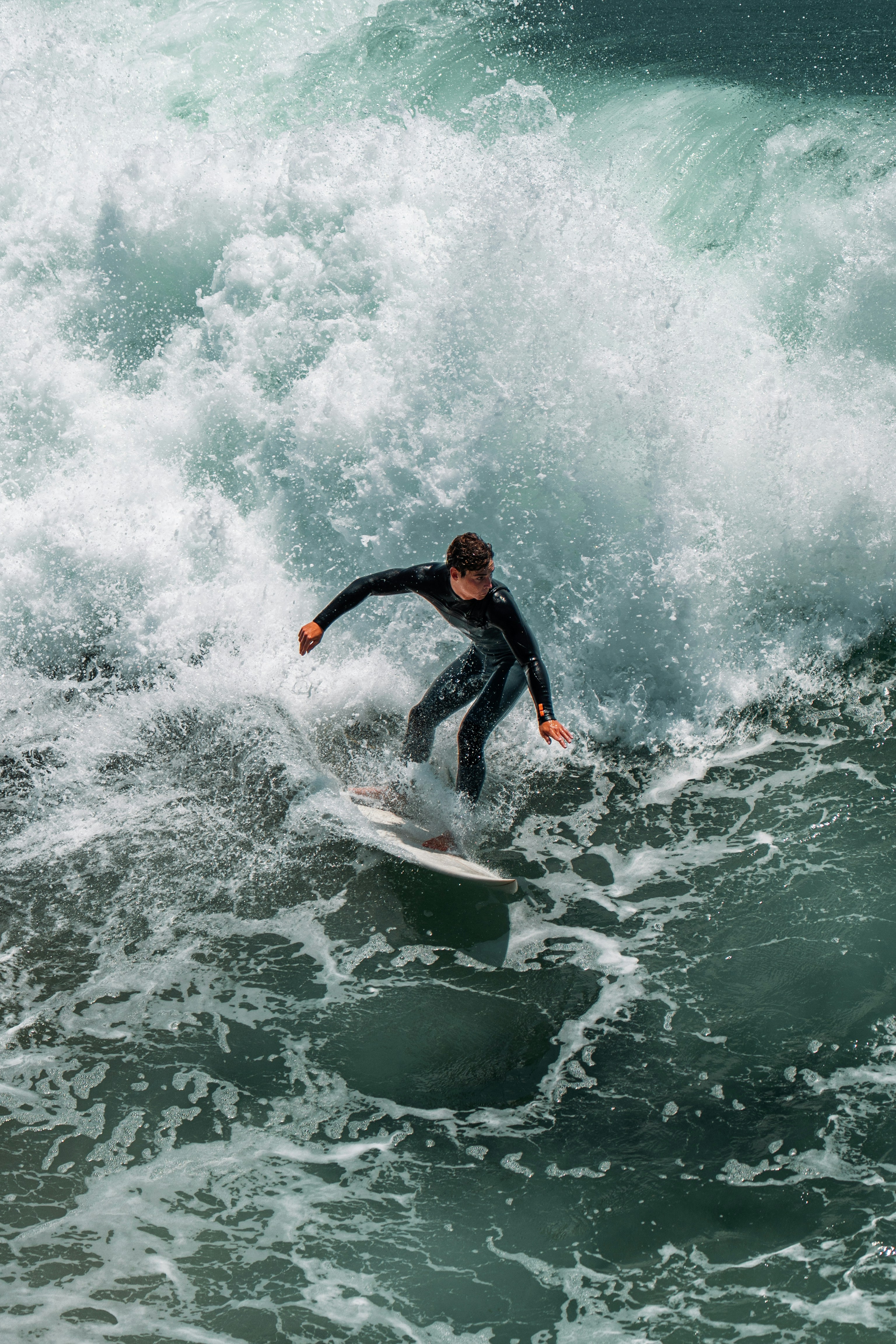 A surfer in a black wetsuit riding a large crashing wave