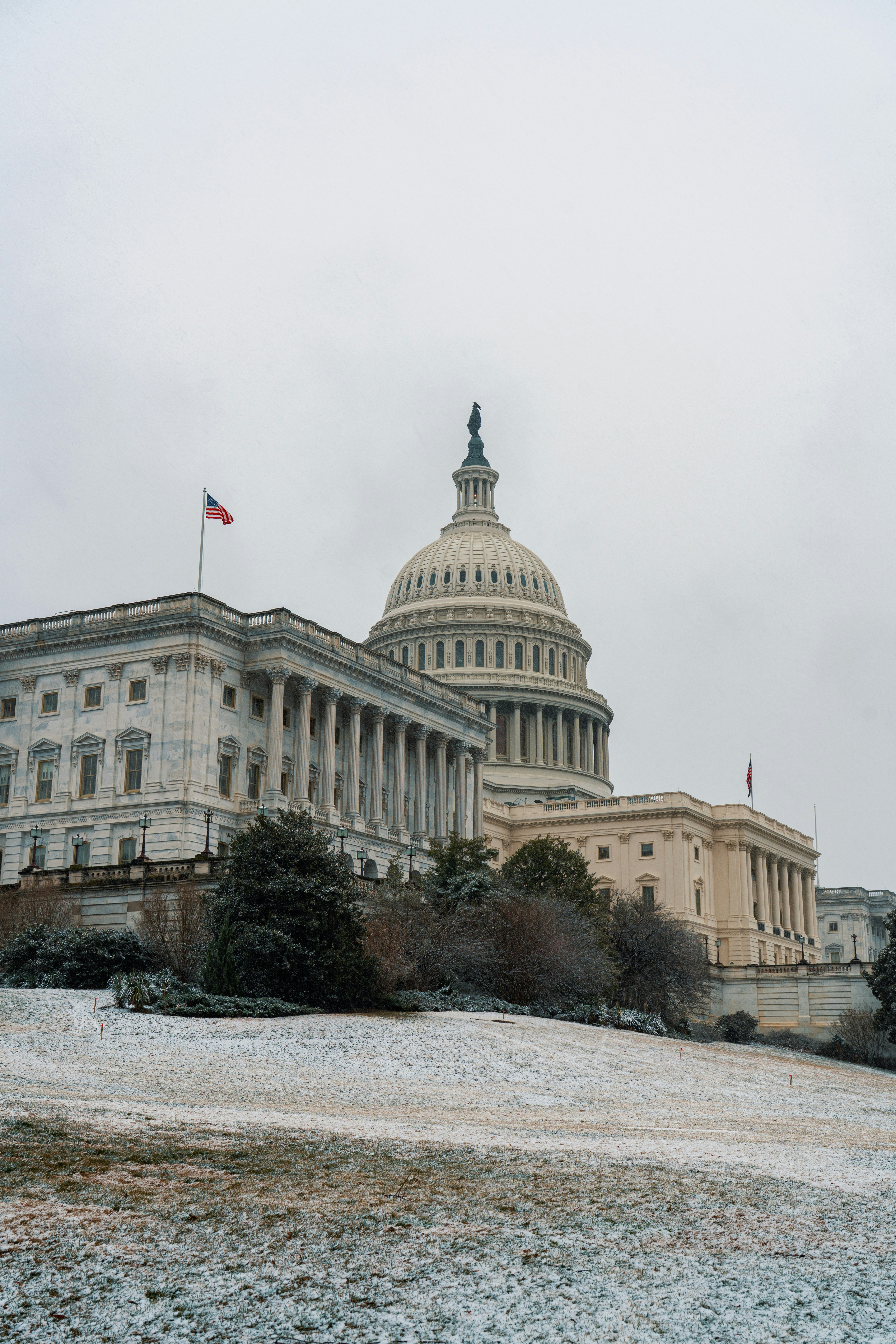 The United States Capitol building under a grey sky with snow on the lawn