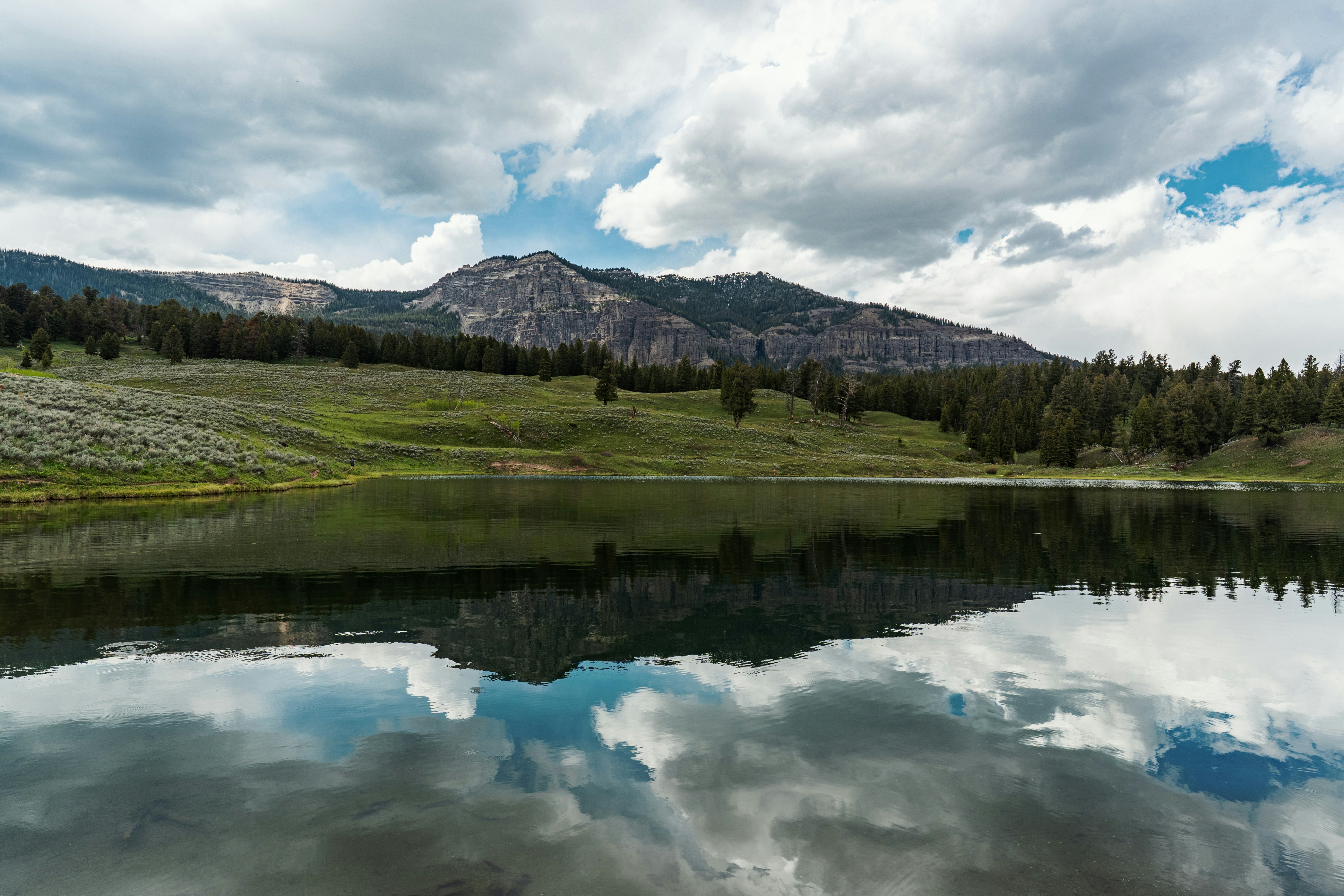 A calm lake reflecting a mountain range and cloudy sky in a green valley