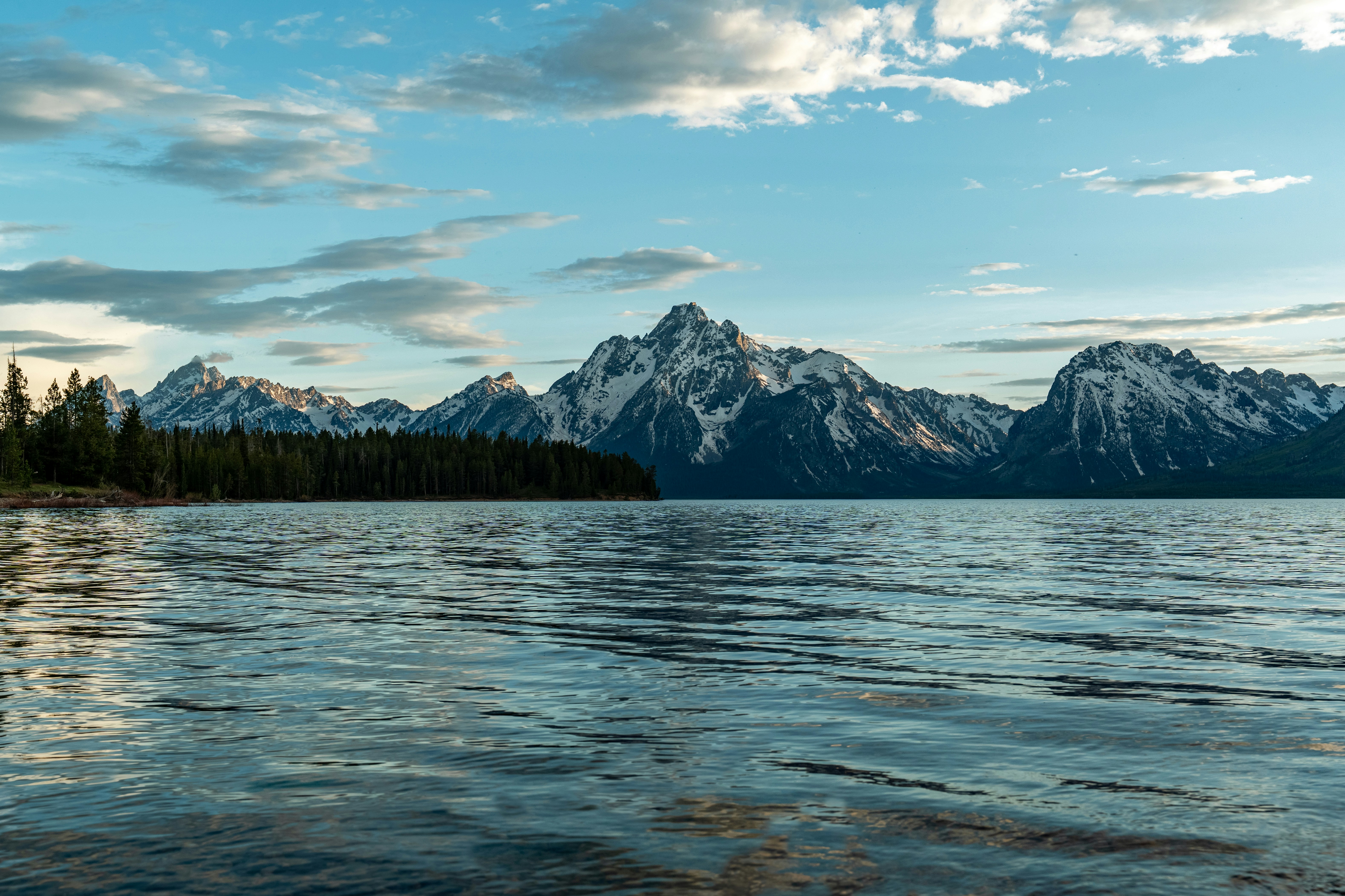 Snow-capped mountains rising above a calm lake with a dark pine forest shoreline