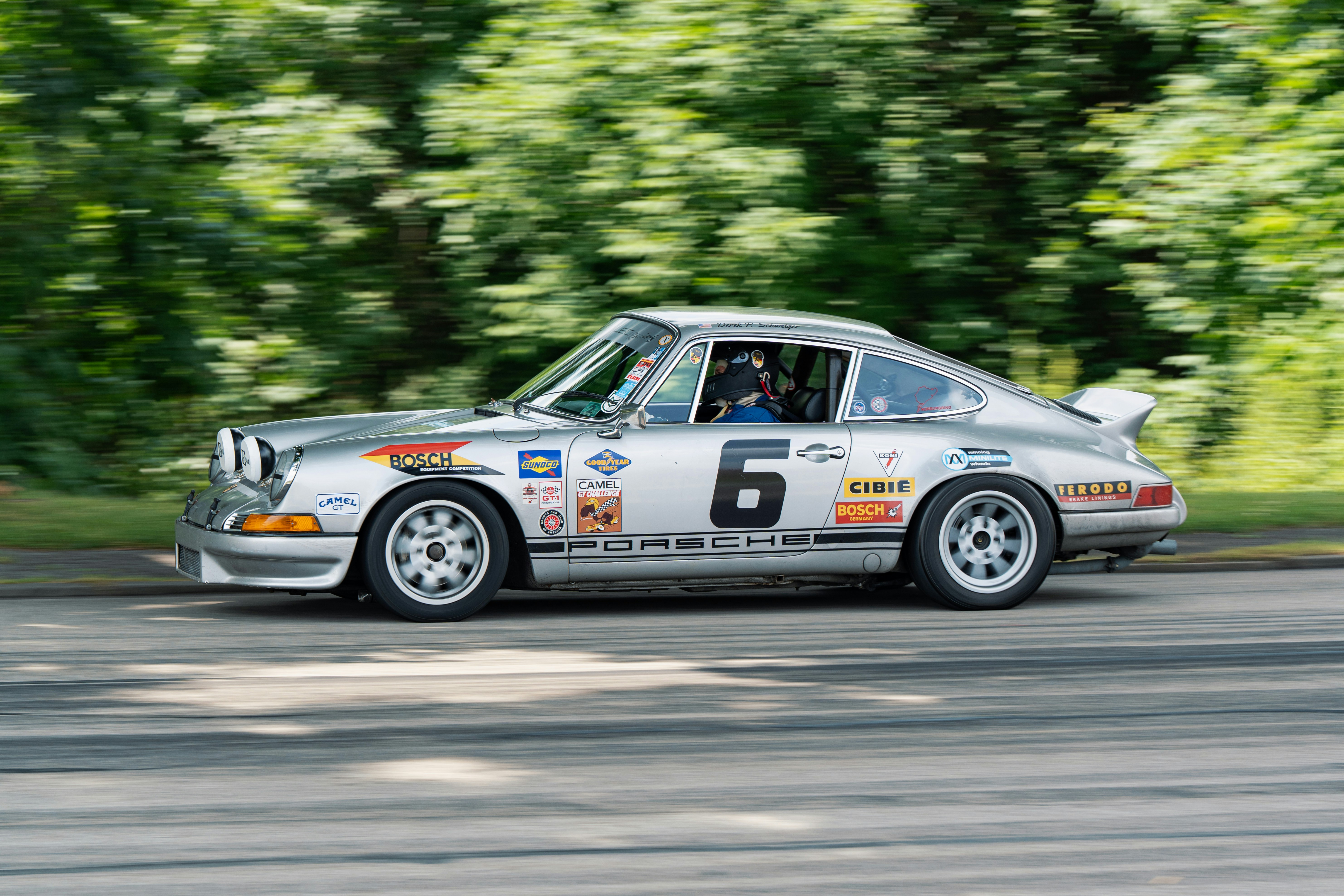 A silver vintage Porsche race car speeding along a track with motion blur