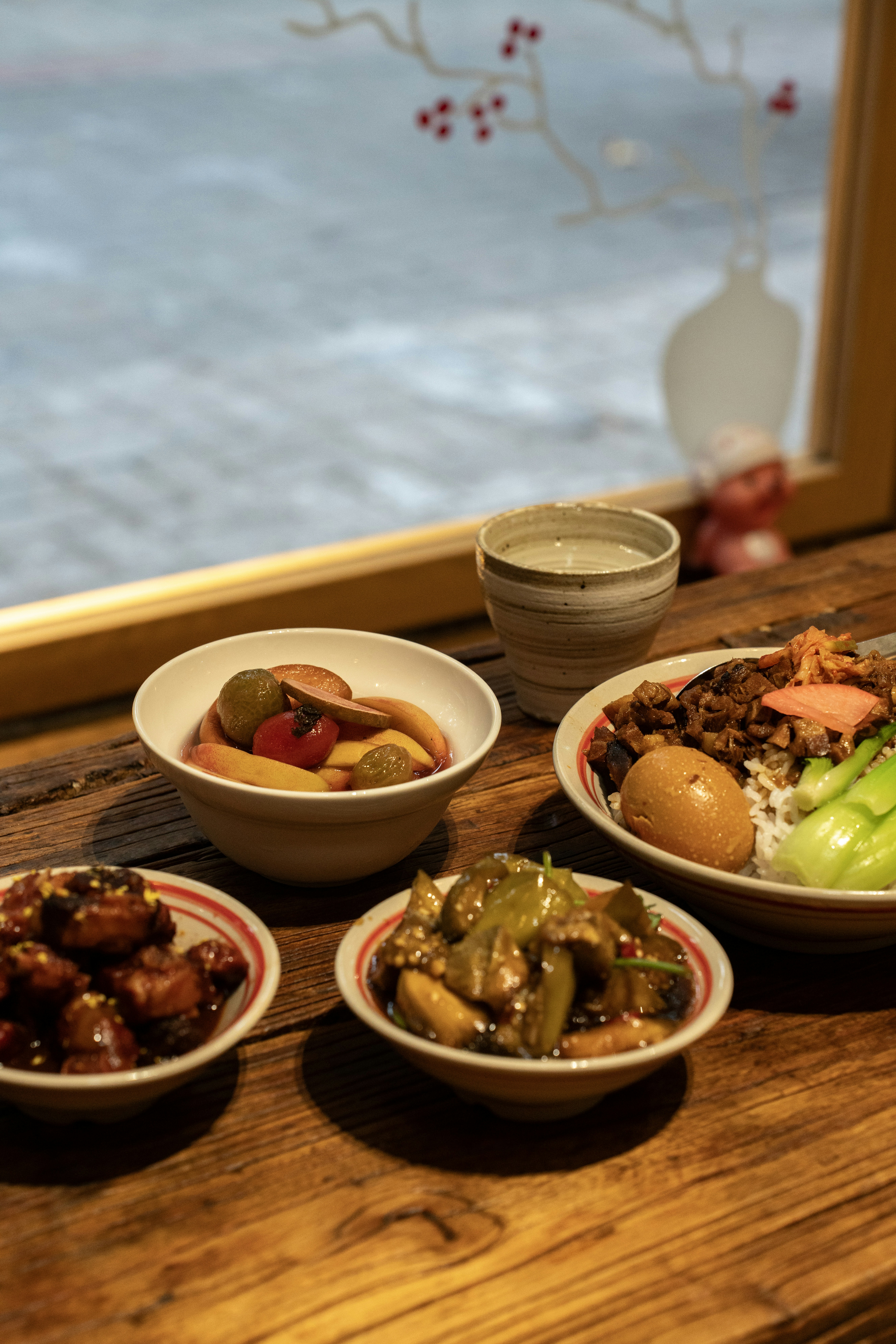 Bowls of braised pork, vegetables, and fruit on a rustic wooden table