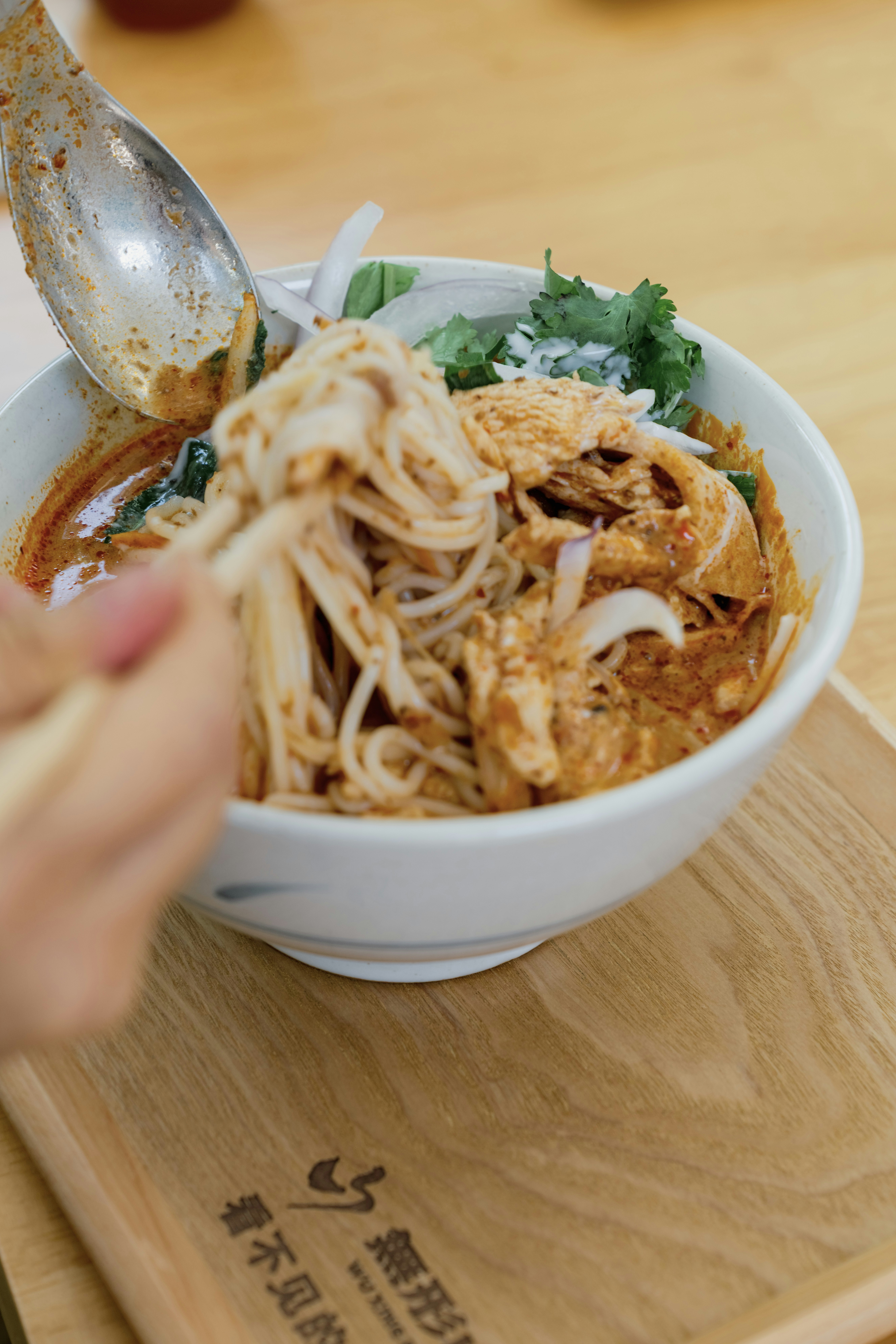 A person using chopsticks to lift rice noodles from a bowl of spicy soup