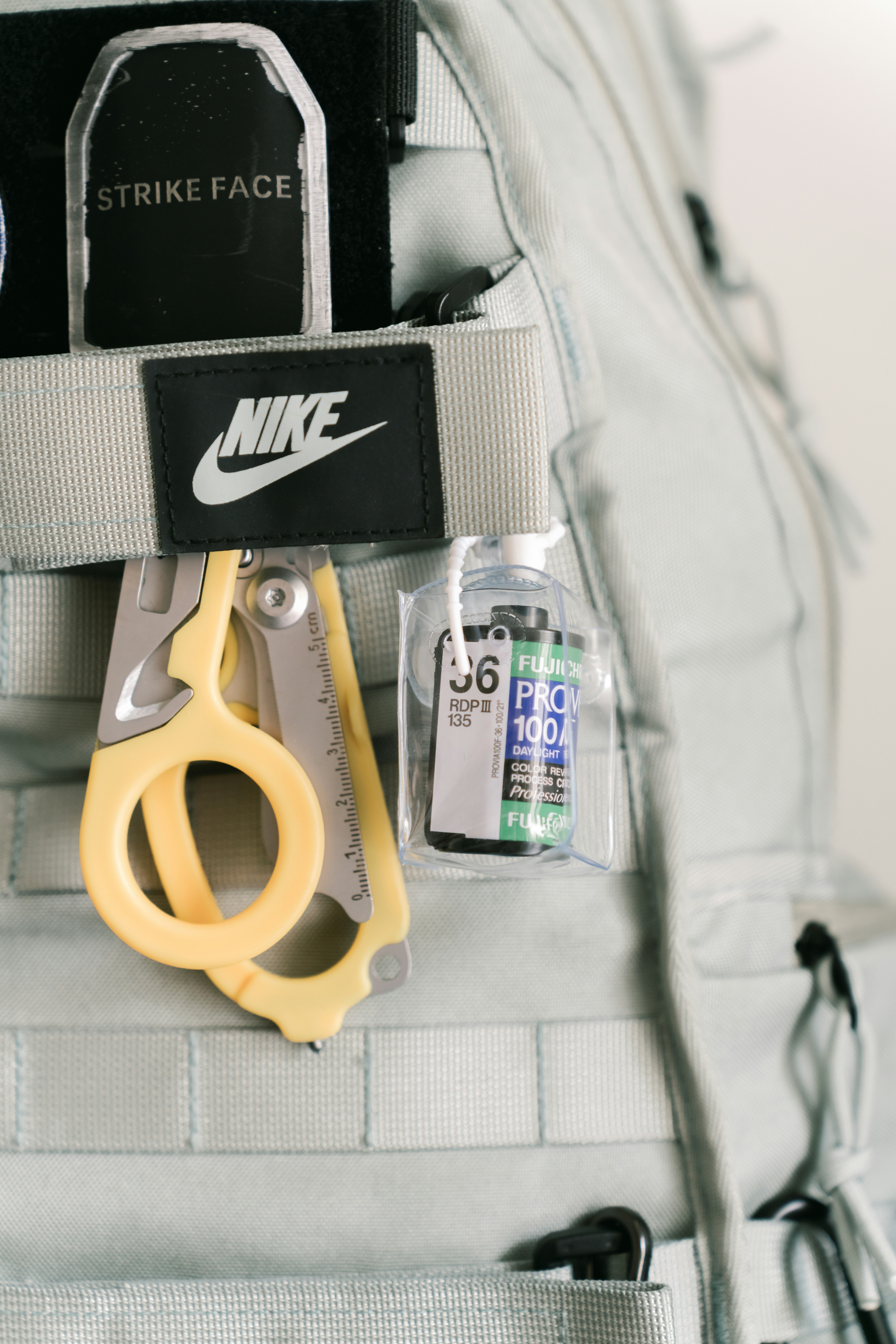 Yellow trauma shears and a roll of 35mm film attached to a grey backpack