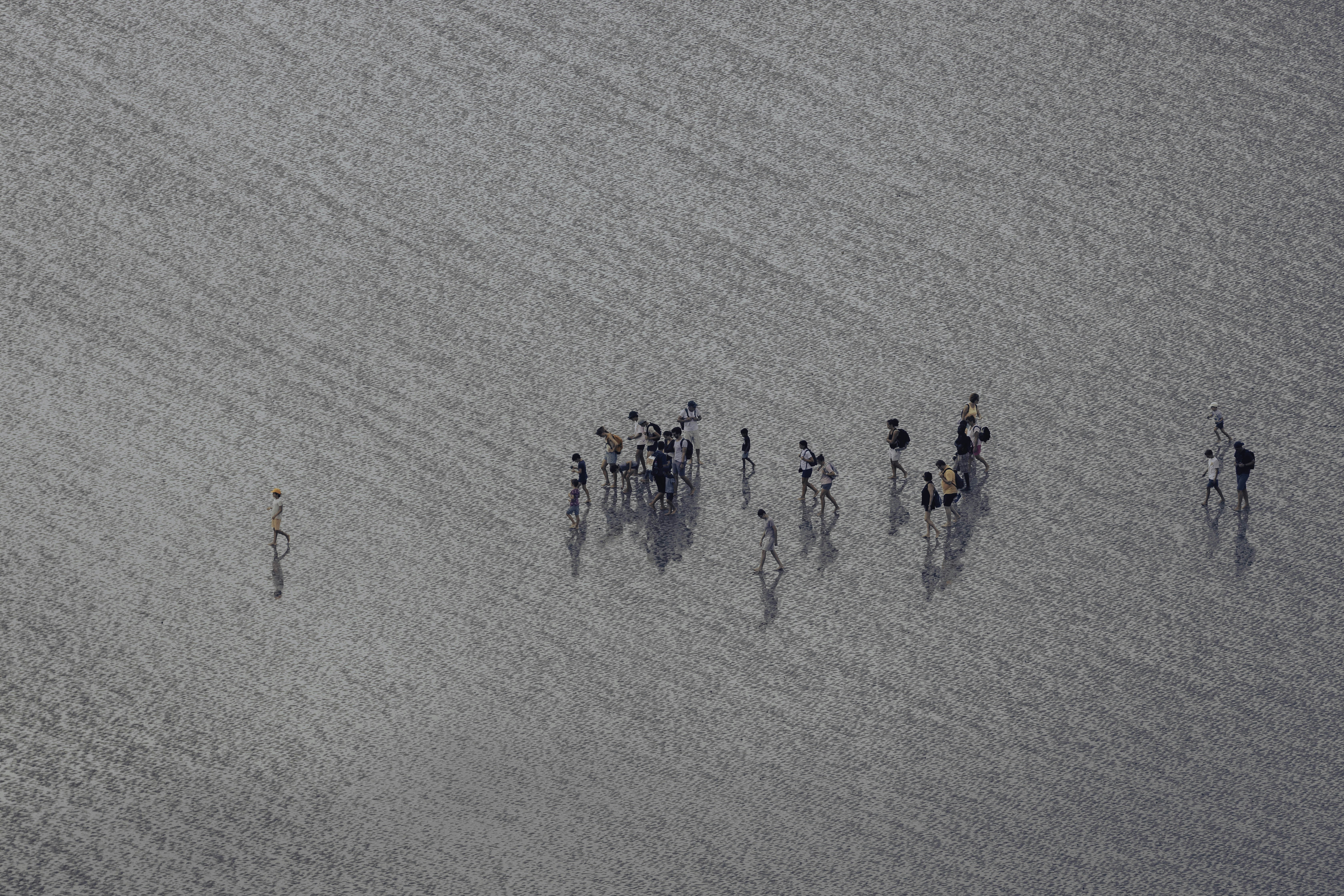 A group of people walking across a vast expanse of wet reflective sand