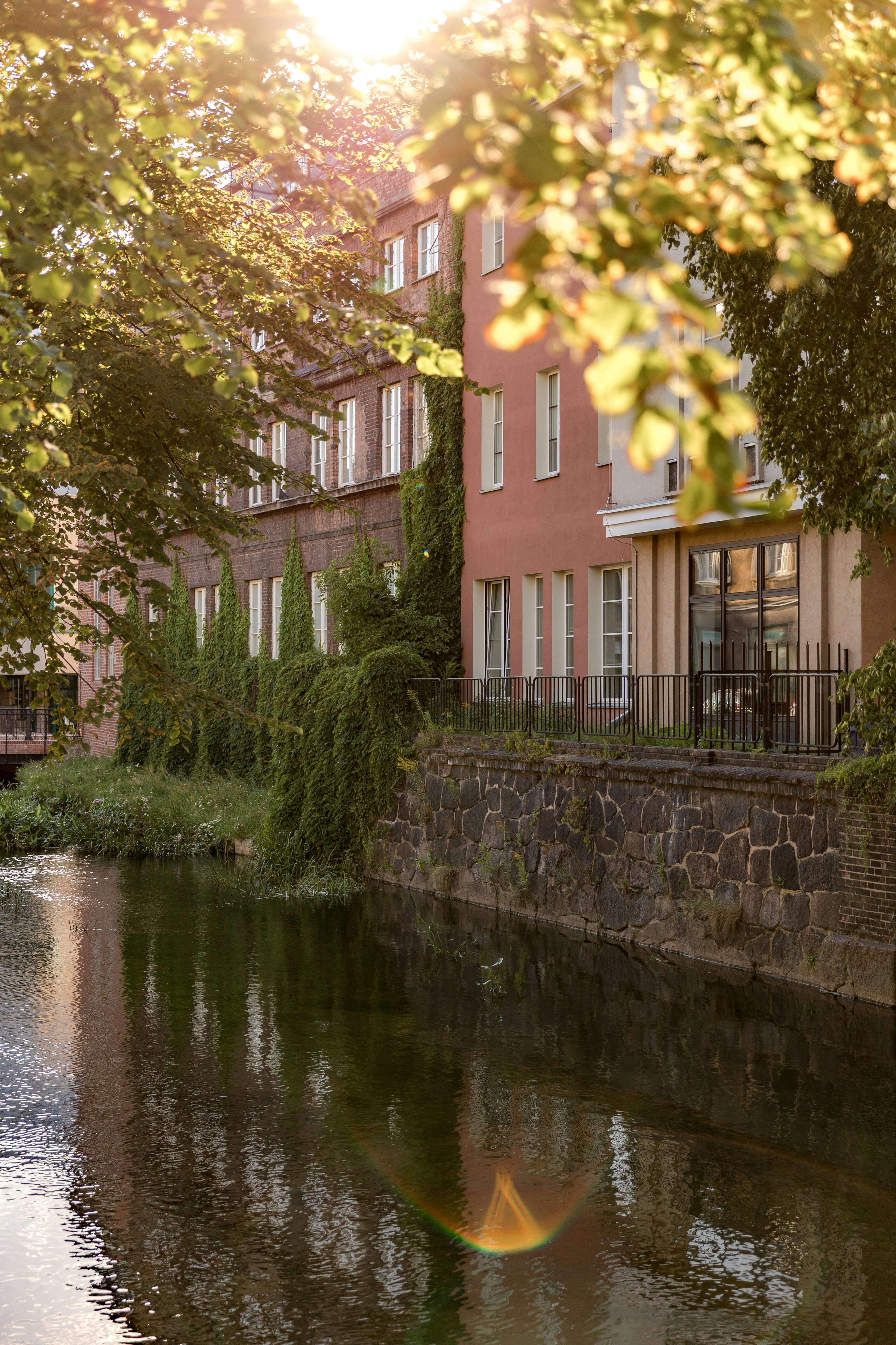 A canal beside a stone wall and buildings with ivy in golden hour light