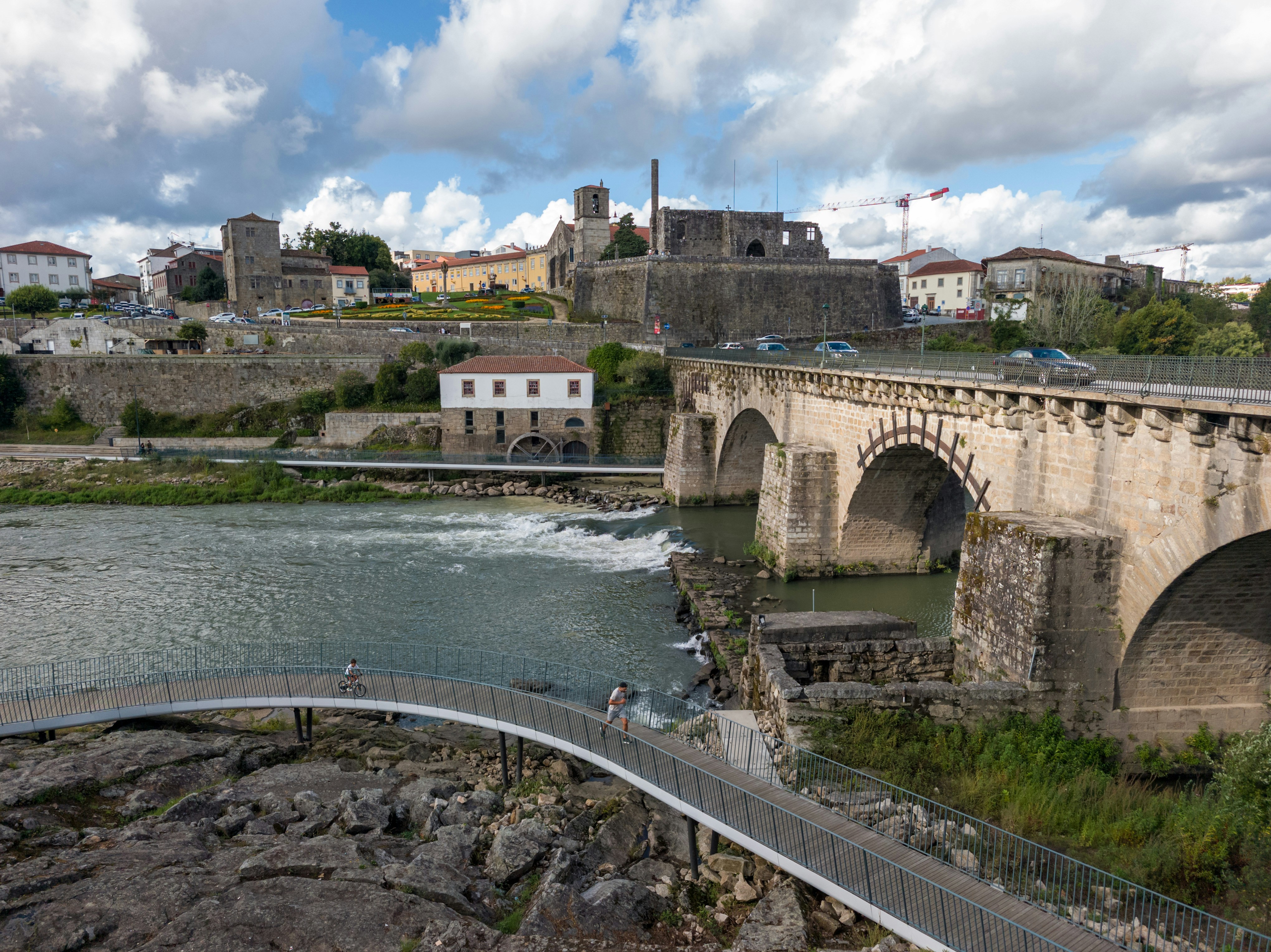 A stone arch bridge over a river with a pedestrian walkway in Barcelos