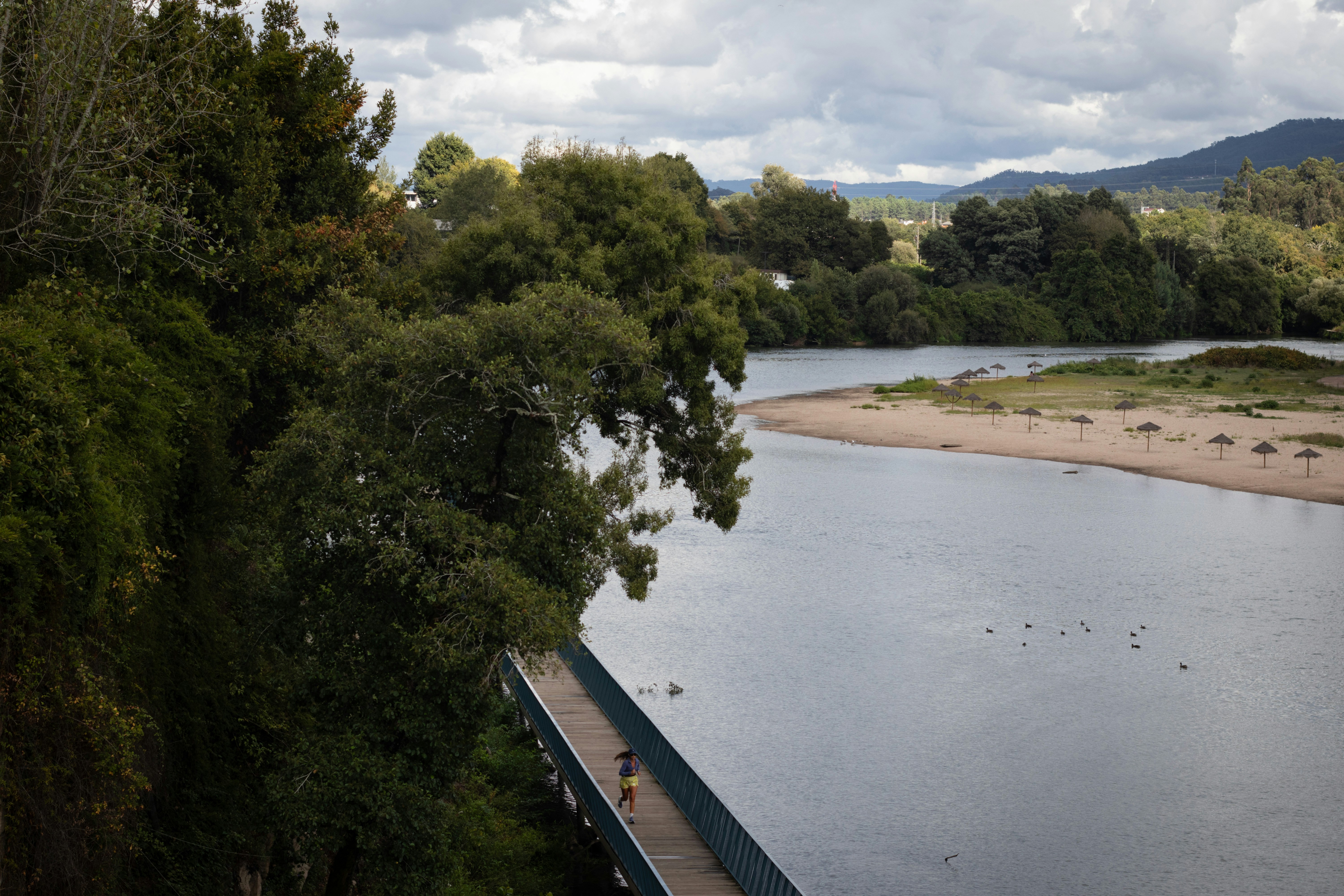 A person running on a wooden boardwalk along a river with a sandy beach