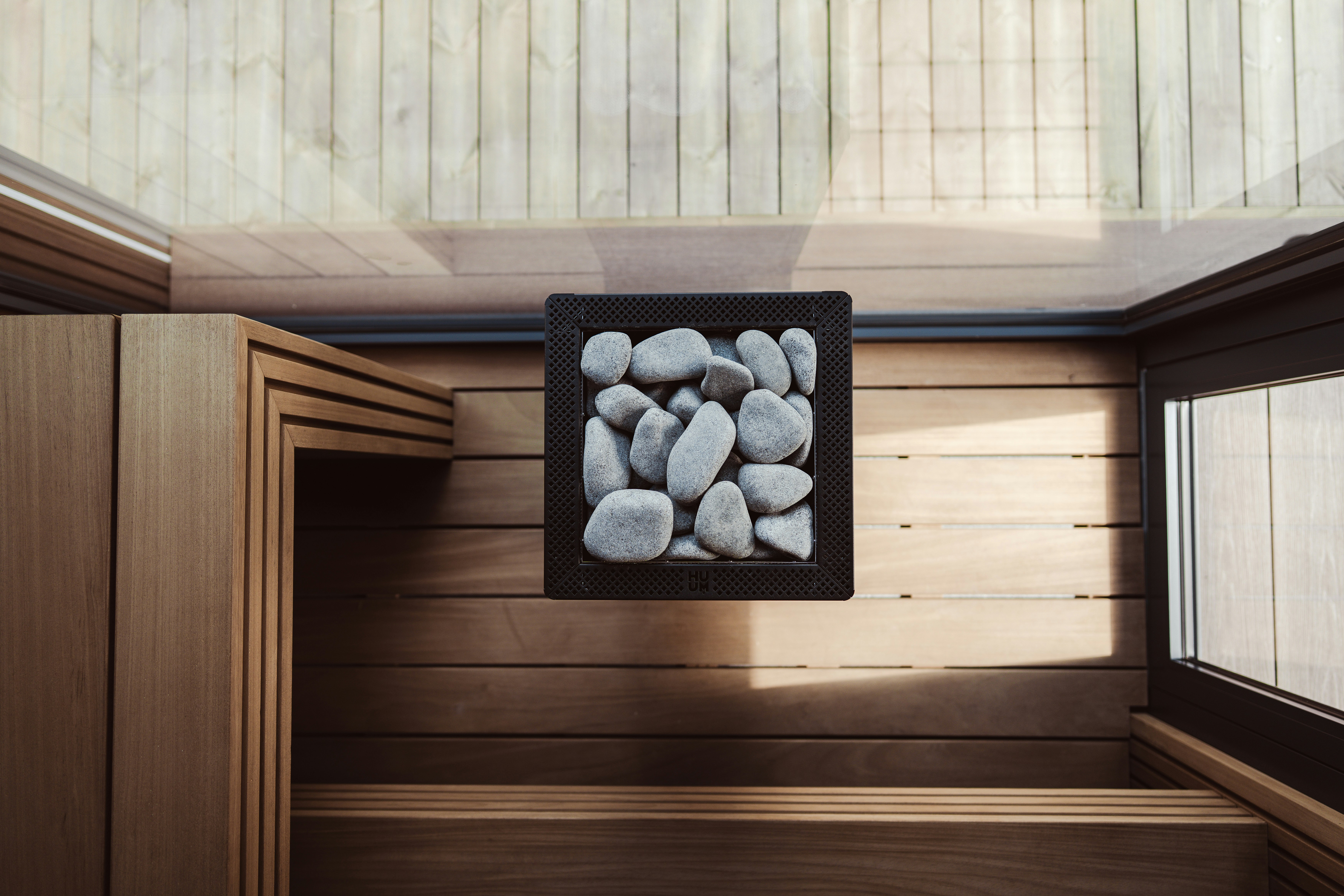Um aquecedor de sauna quadrado cheio de pedras cinzas sobre um piso de madeira