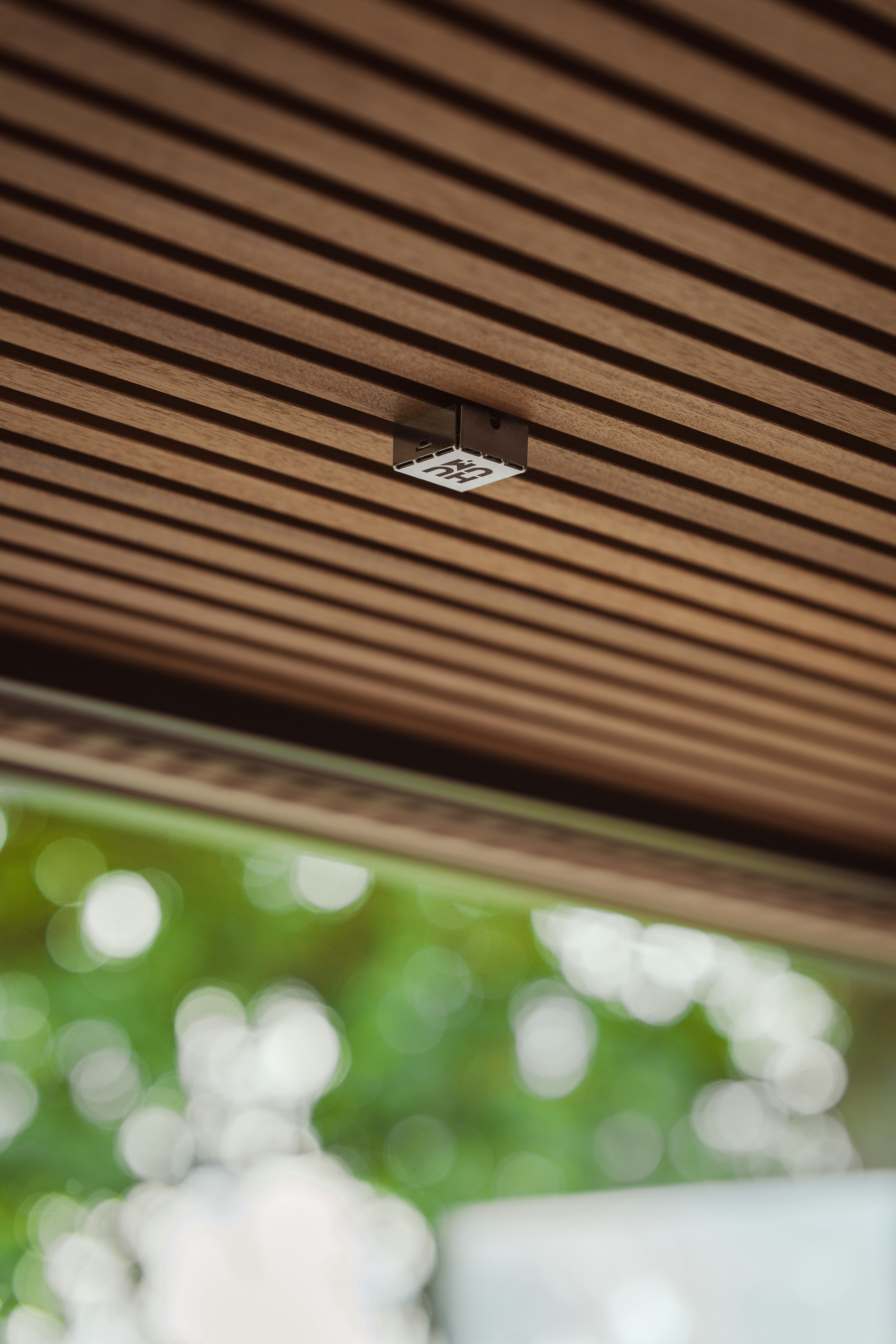 Um pequeno sensor metálico quadrado montado em um teto de madeira com ripas