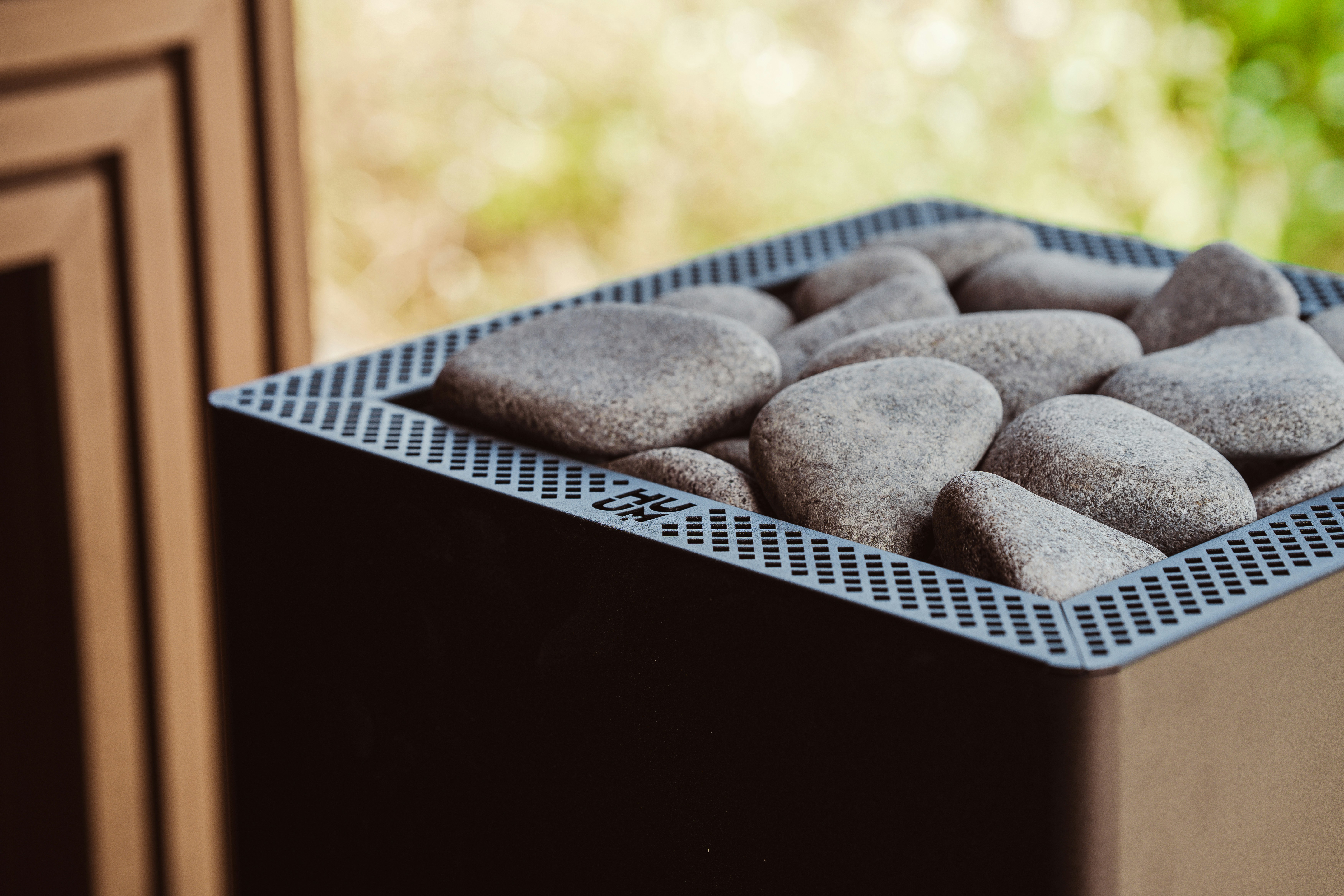 Pedras cinza lisas dentro de um aquecedor de sauna de metal preto com tampa perfurada