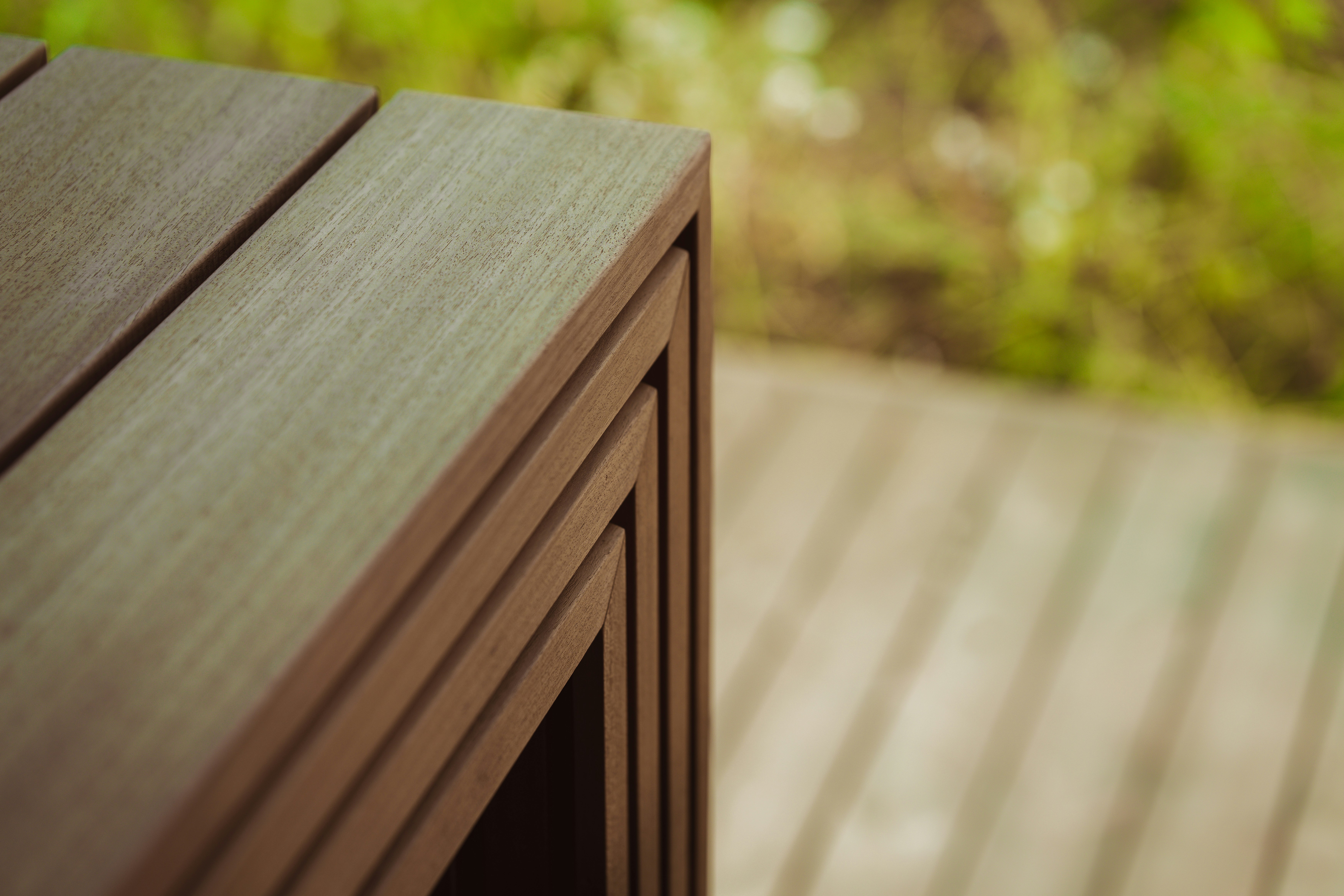 A stack of three nested wooden tables on a deck with blurred greenery