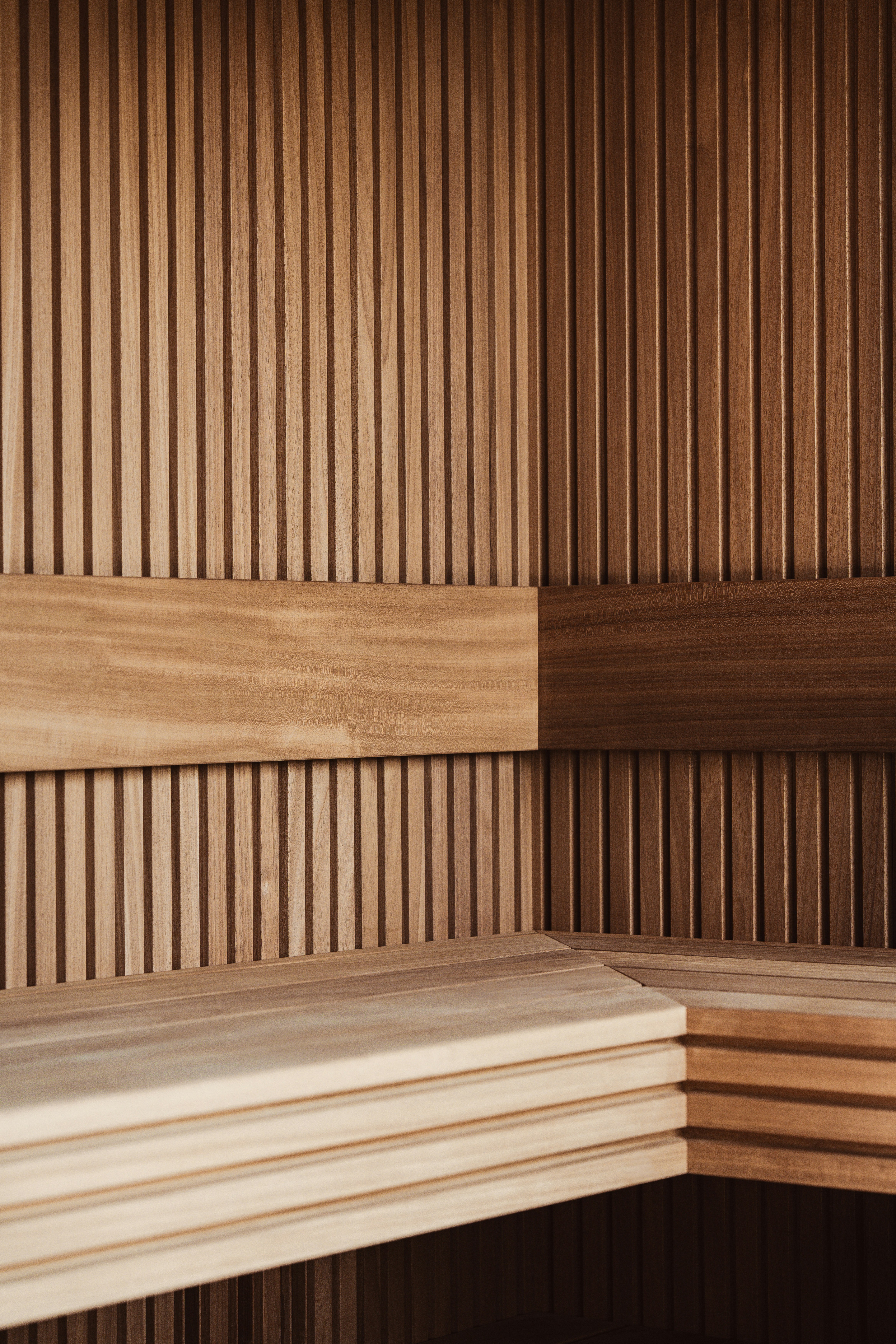 Um canto de uma sauna com ripas verticais de madeira e tábuas horizontais para bancos