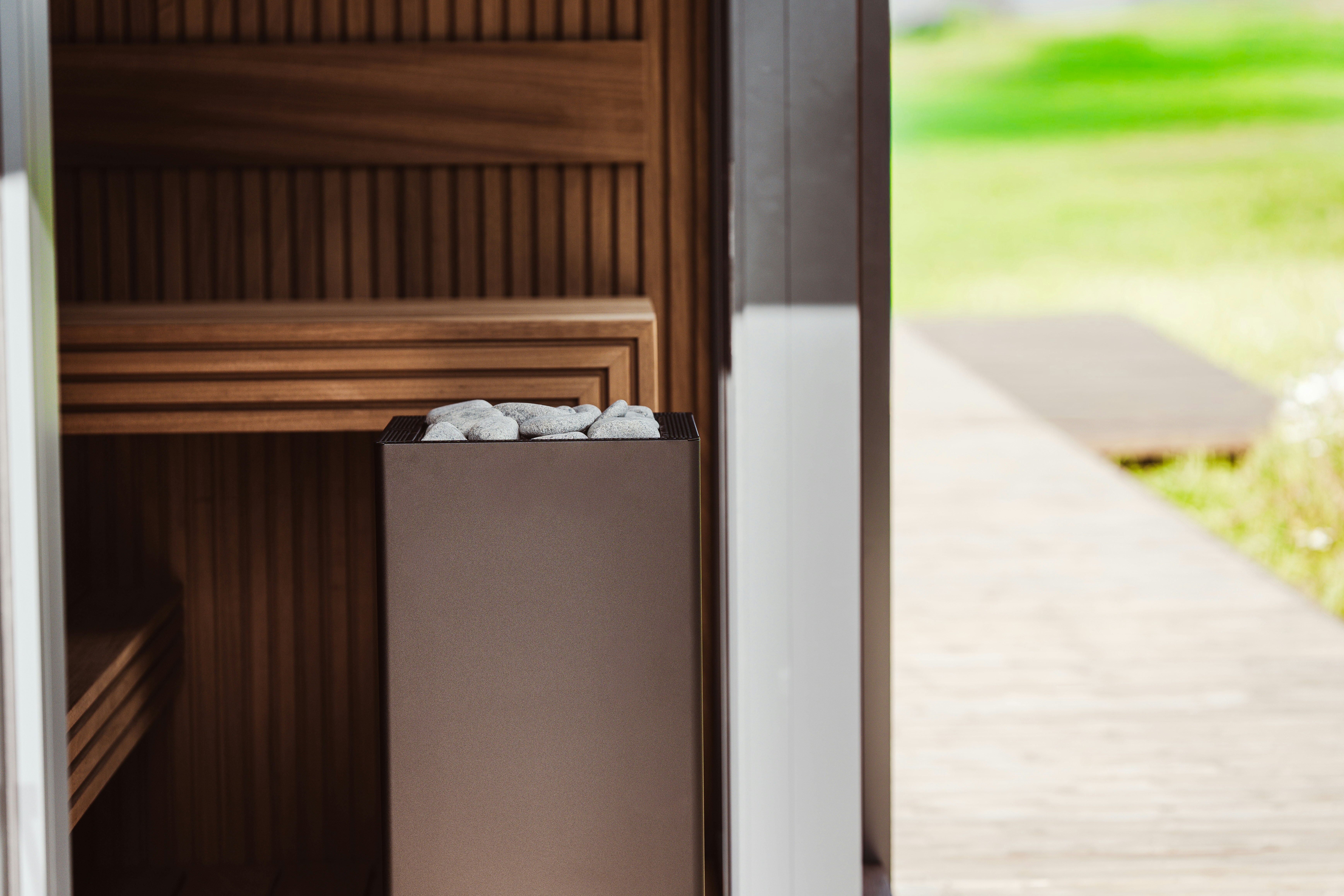 Um aquecedor de sauna com pedras cinzas dentro de um cômodo de madeira com porta de vidro