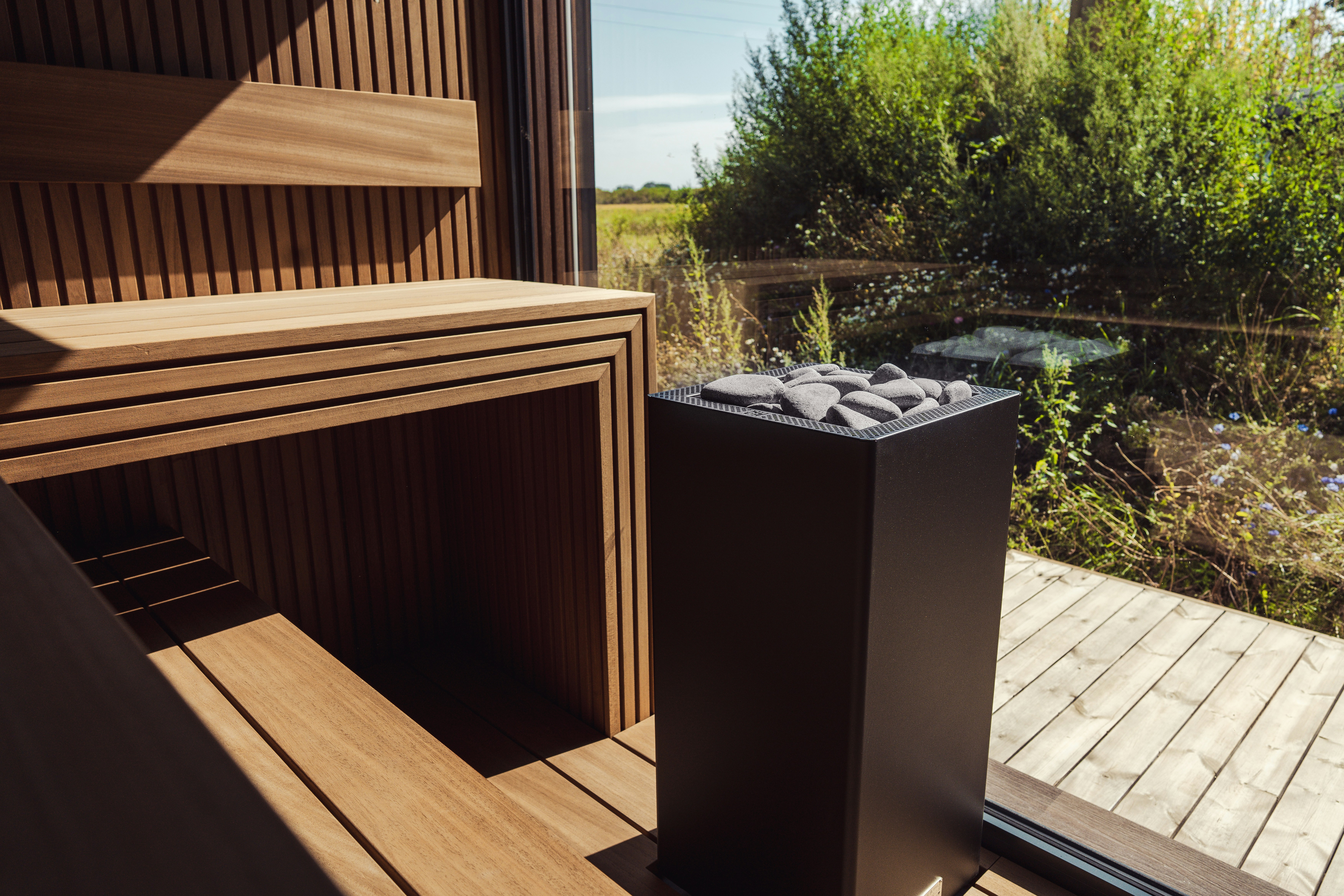 Um aquecedor de sauna preto com pedras cinza dentro de uma sauna de madeira