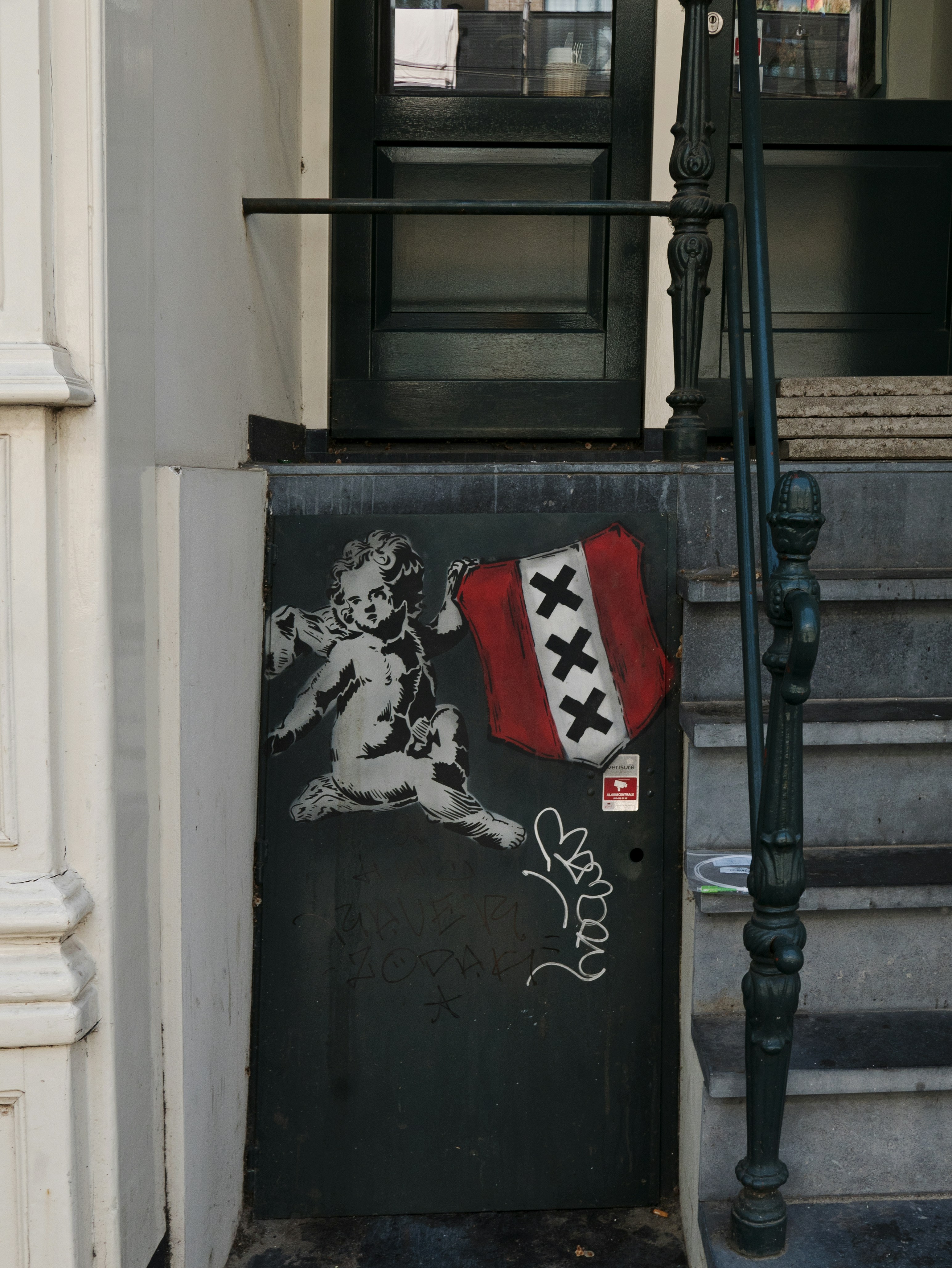 A stencil of a cherub holding the Amsterdam flag on a dark door