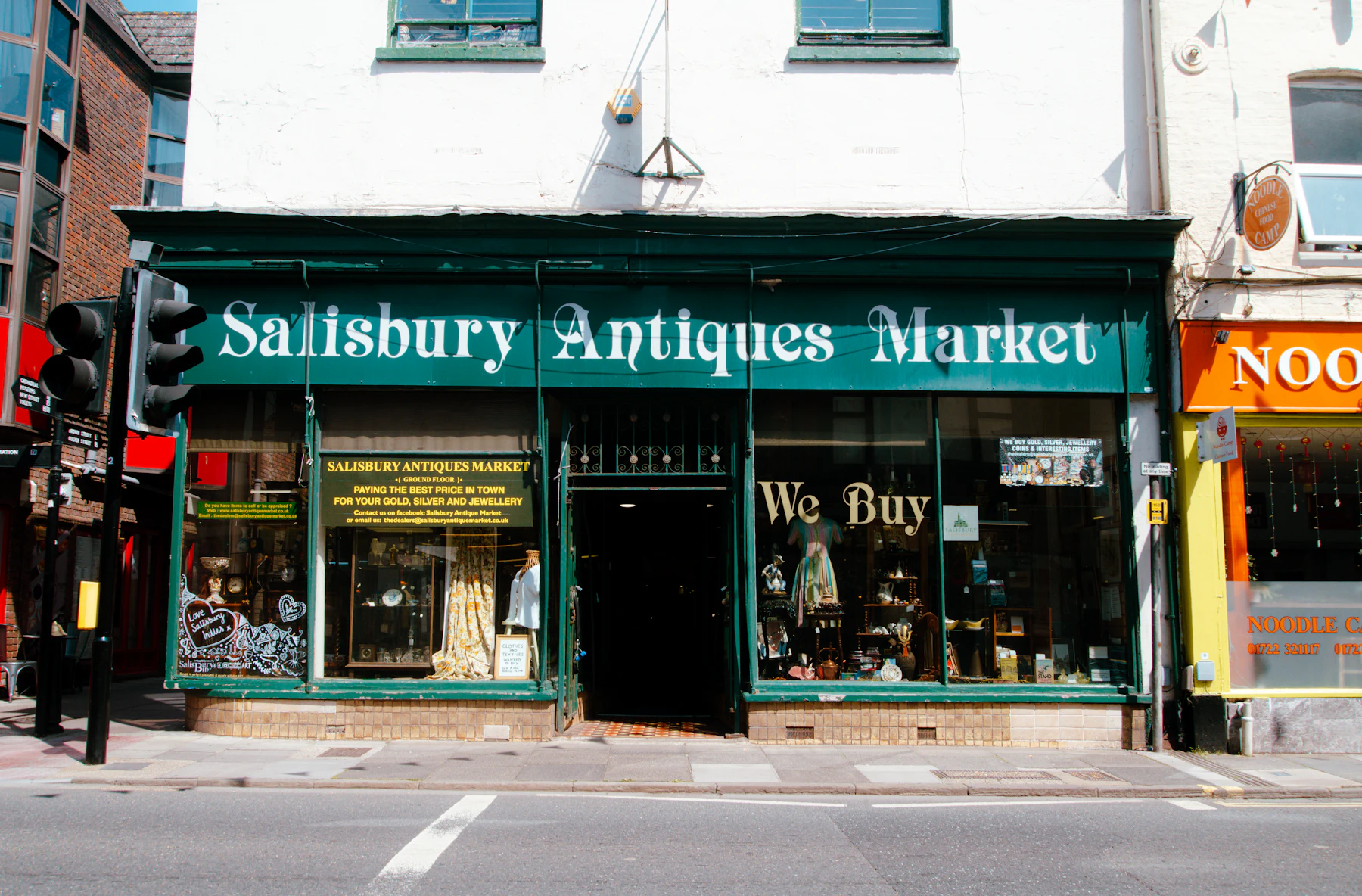 A green antiques market storefront with large display windows on a town street