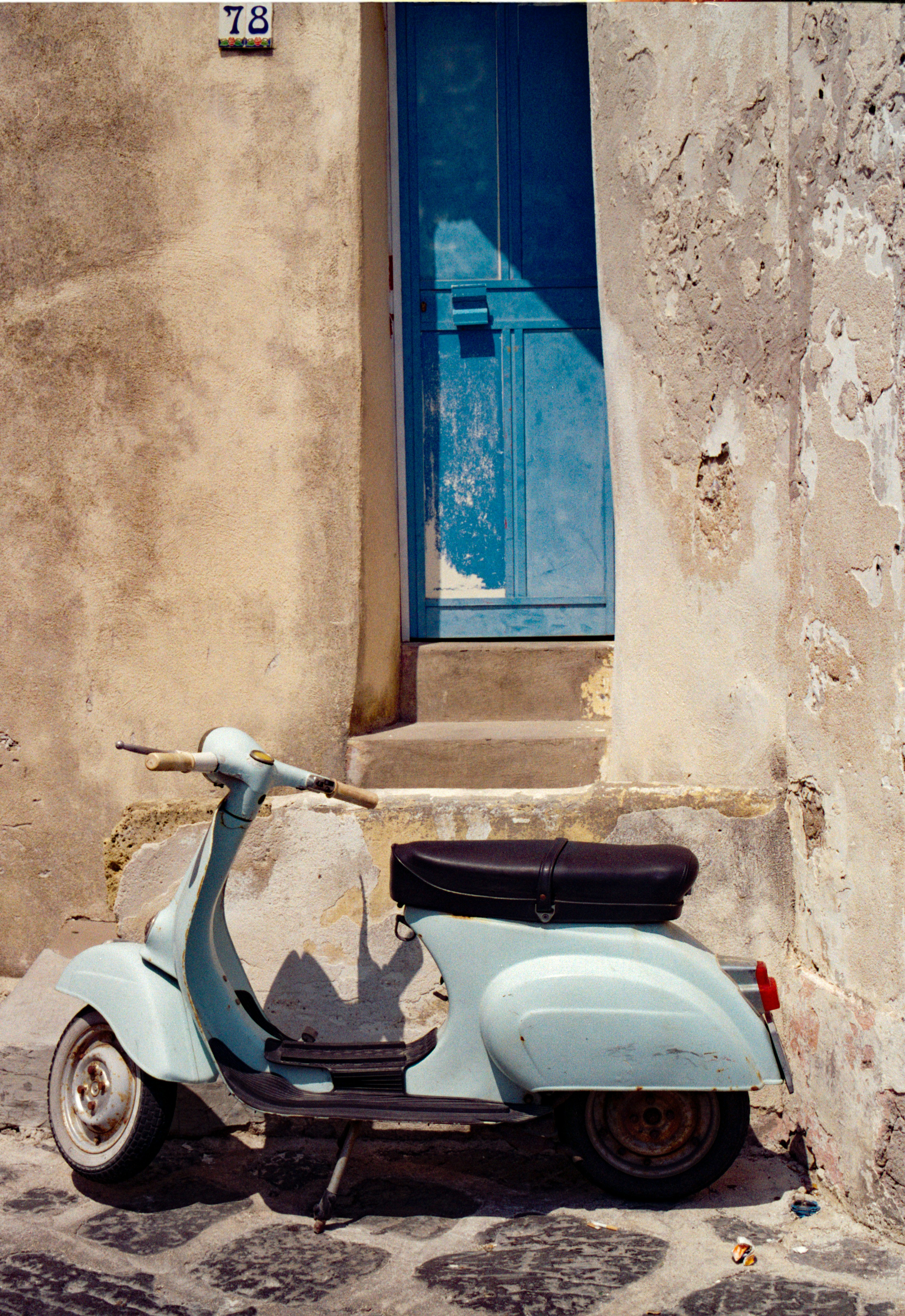 Un scooter vintage azul claro aparcado frente a una puerta azul en una pared desgastada