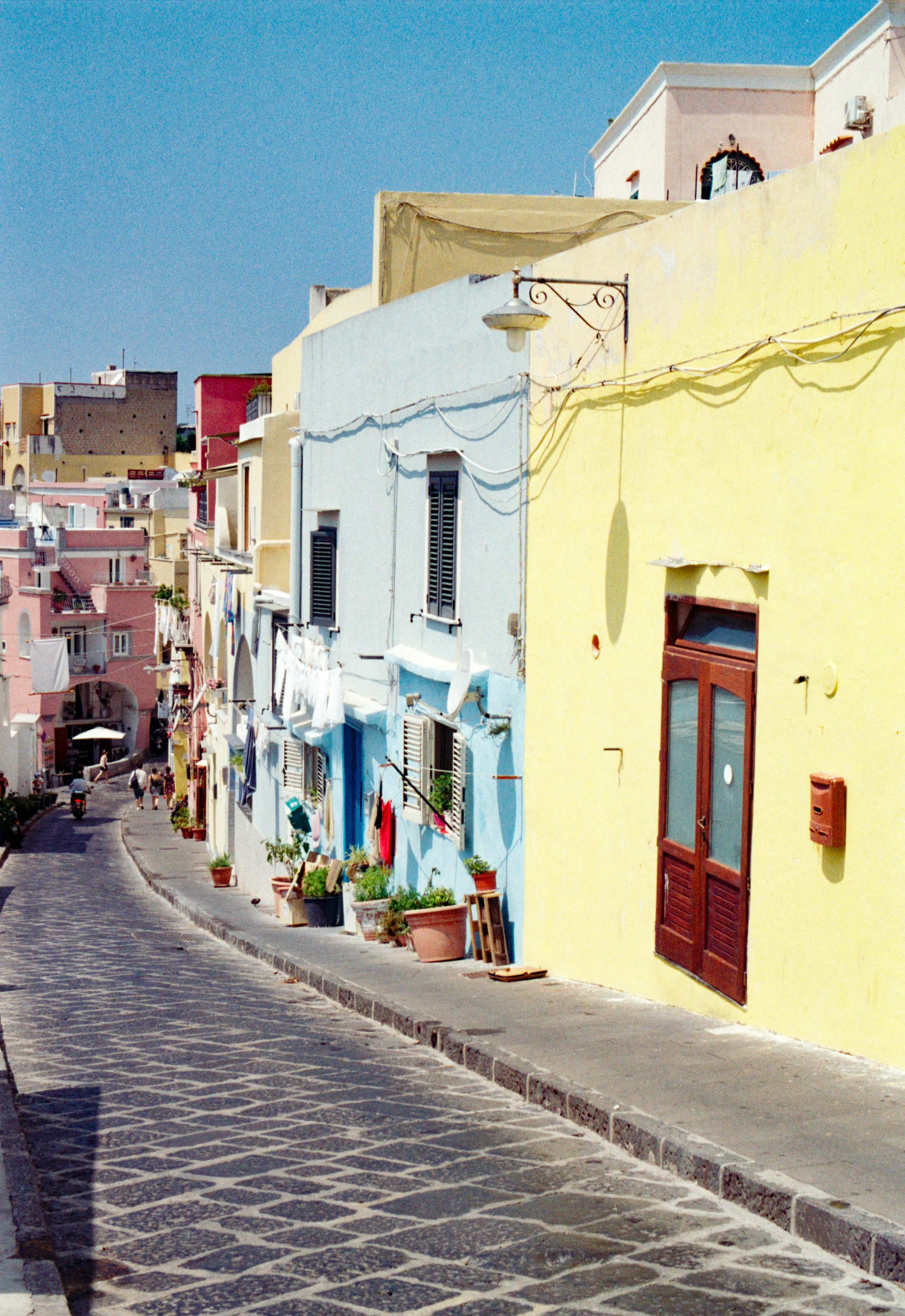 Una calle estrecha de adoquines bordeada de edificios coloridos en amarillo y azul en Procida, Italia