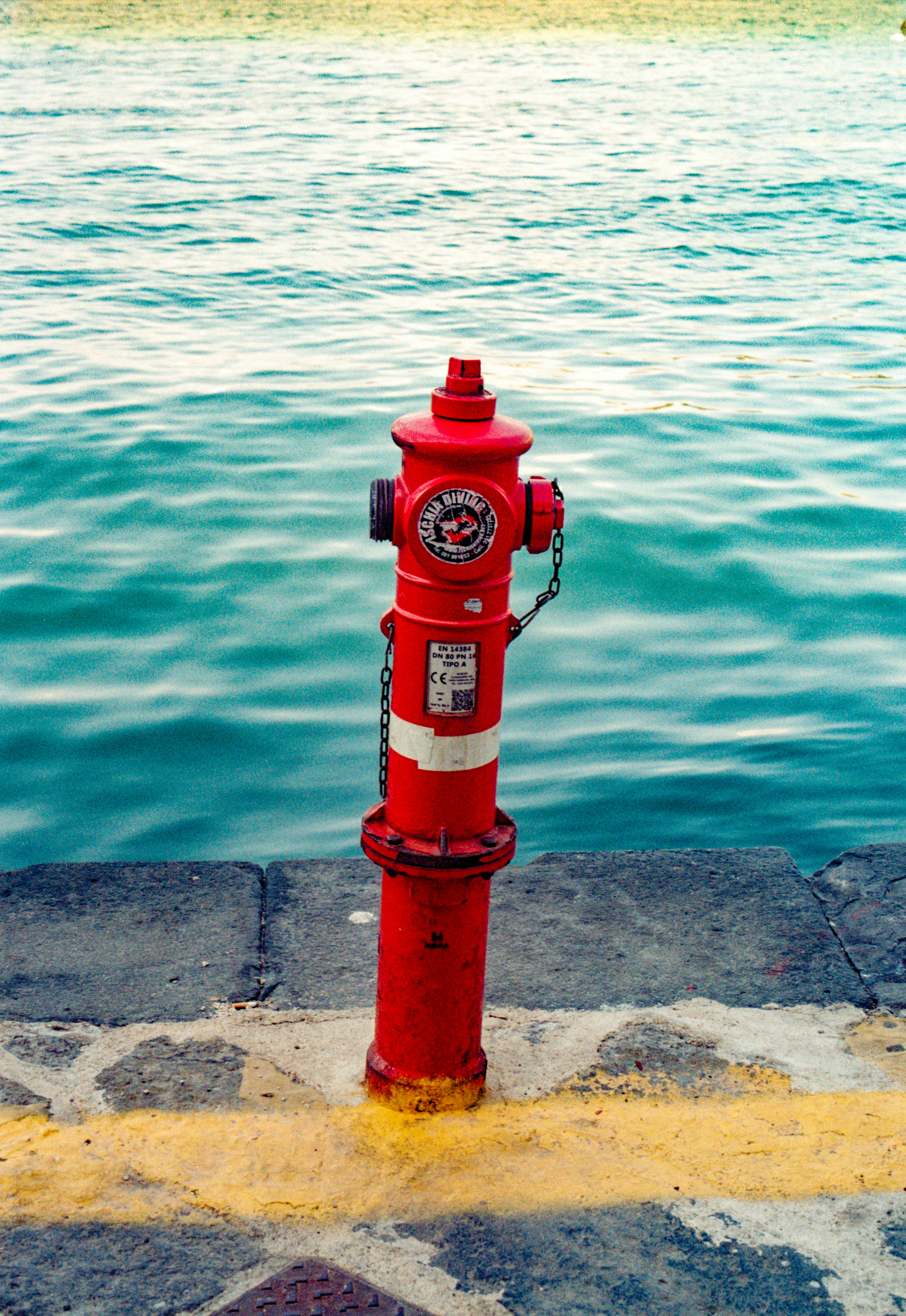 Una boca de incendios roja en un muelle de piedra junto a aguas azules