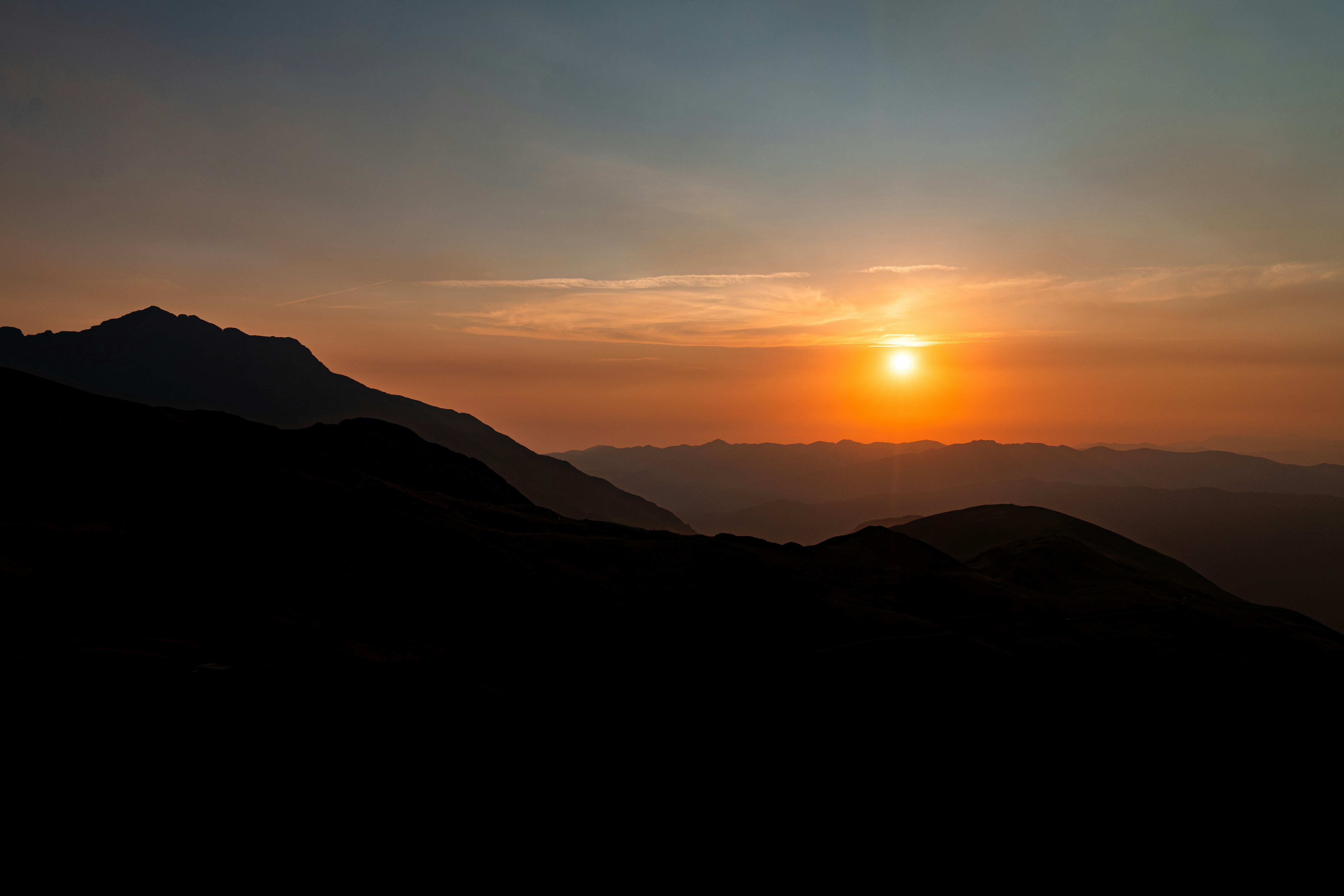 Silhouetted mountain ridges against a warm orange sky with a low sun