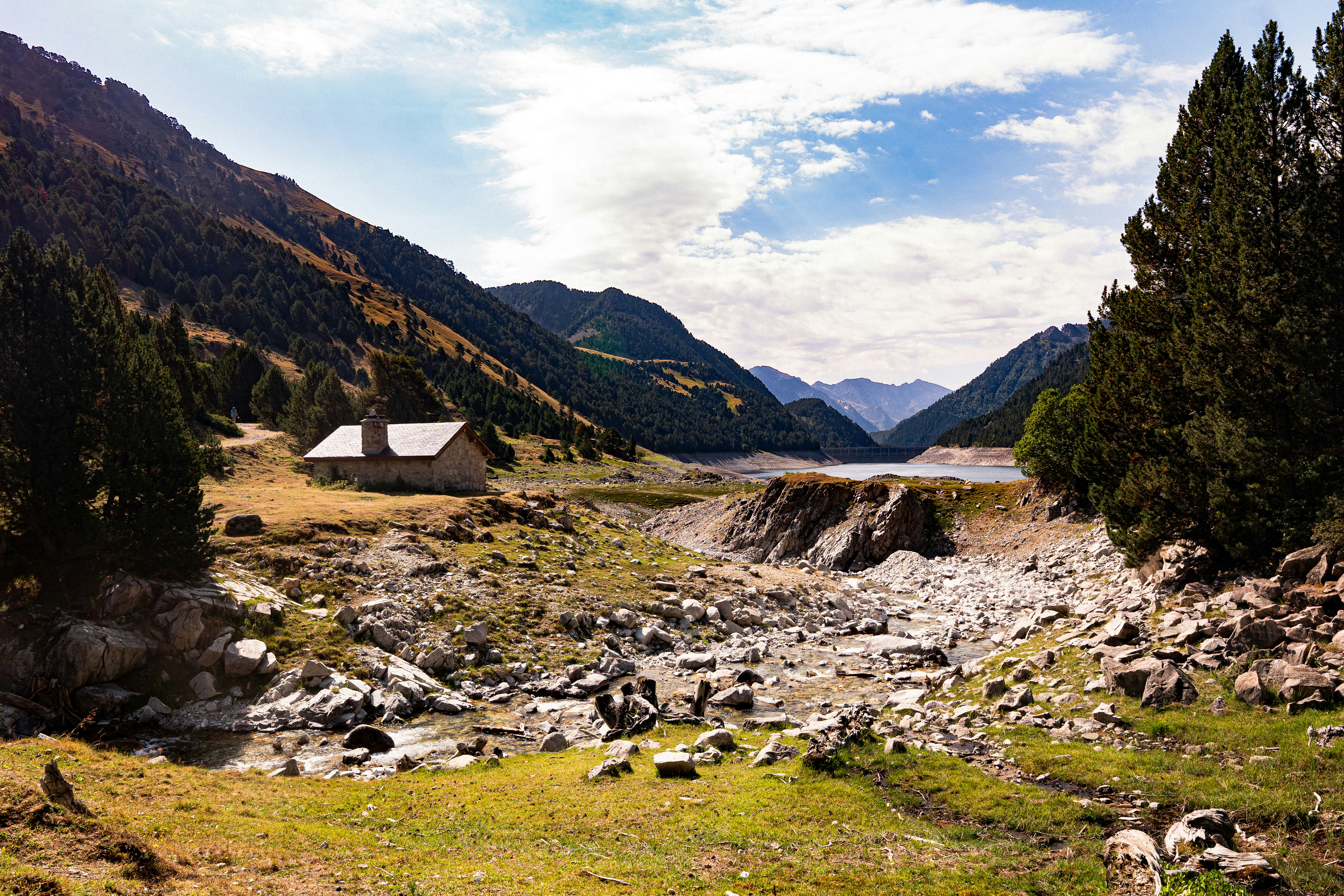 A stone cabin on a grassy slope above a rocky stream in the mountains