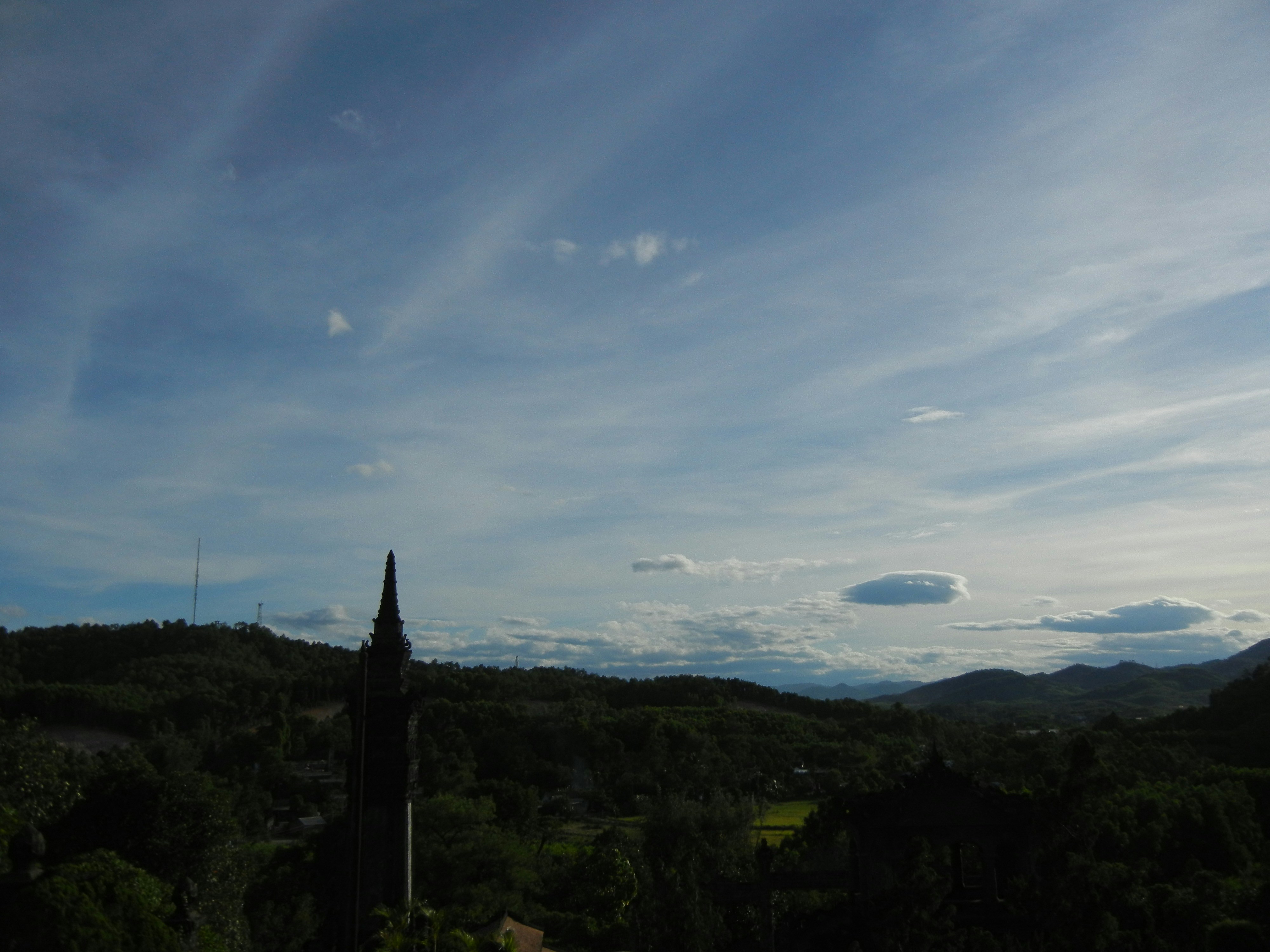 A tall dark spire rising above a forested valley under a blue sky
