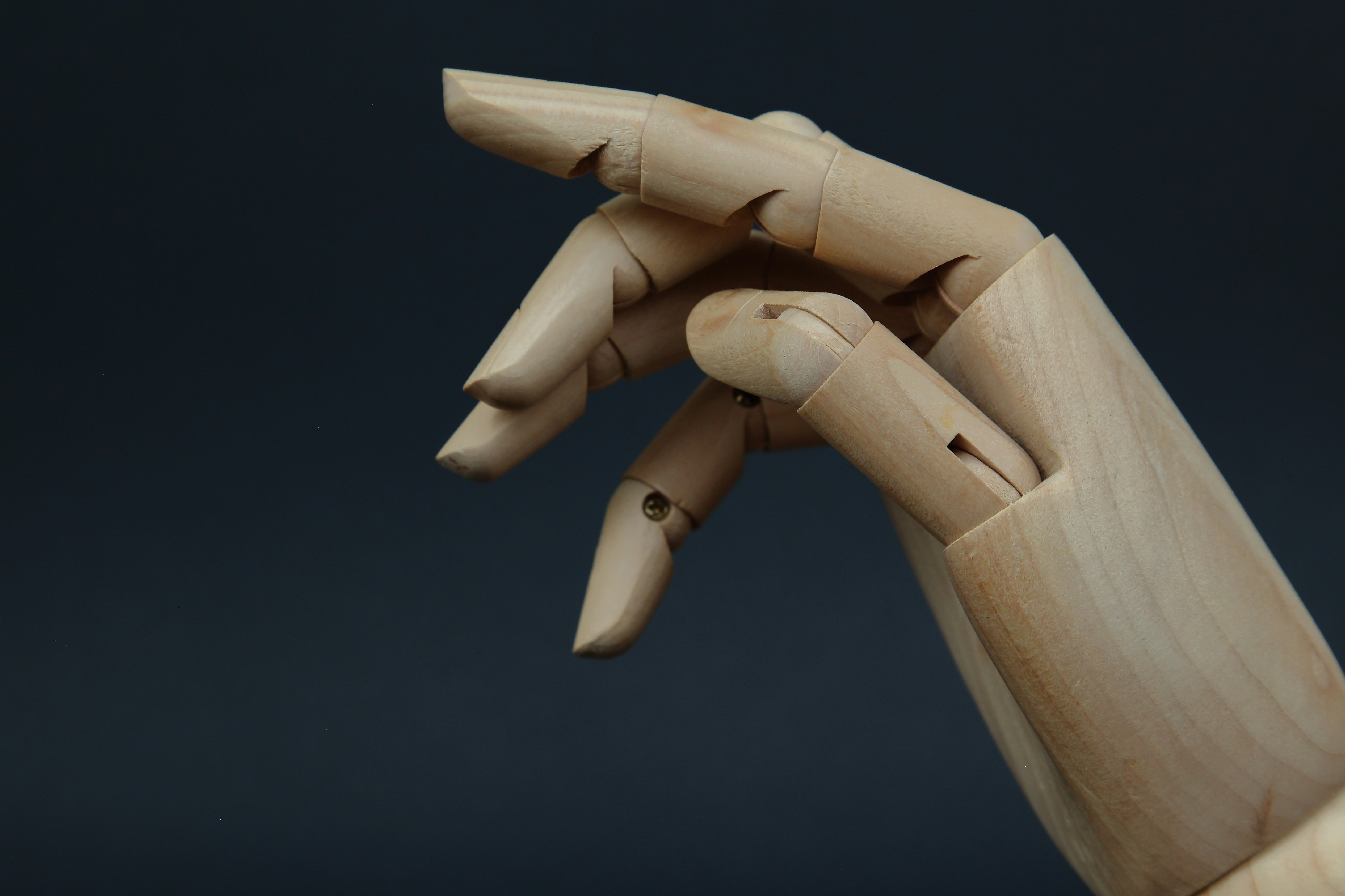 A wooden mannequin hand with articulated fingers against a dark grey background
