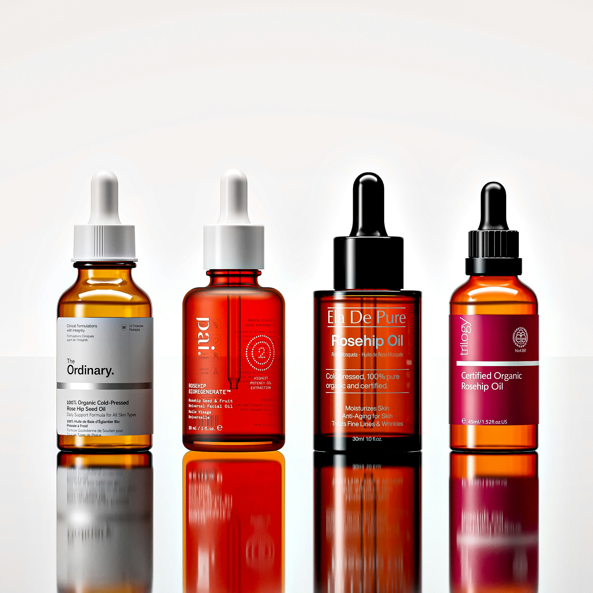 Four amber glass dropper bottles of facial oil on a reflective white surface