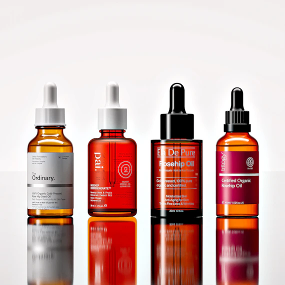 Four amber glass dropper bottles of facial oil on a reflective white surface