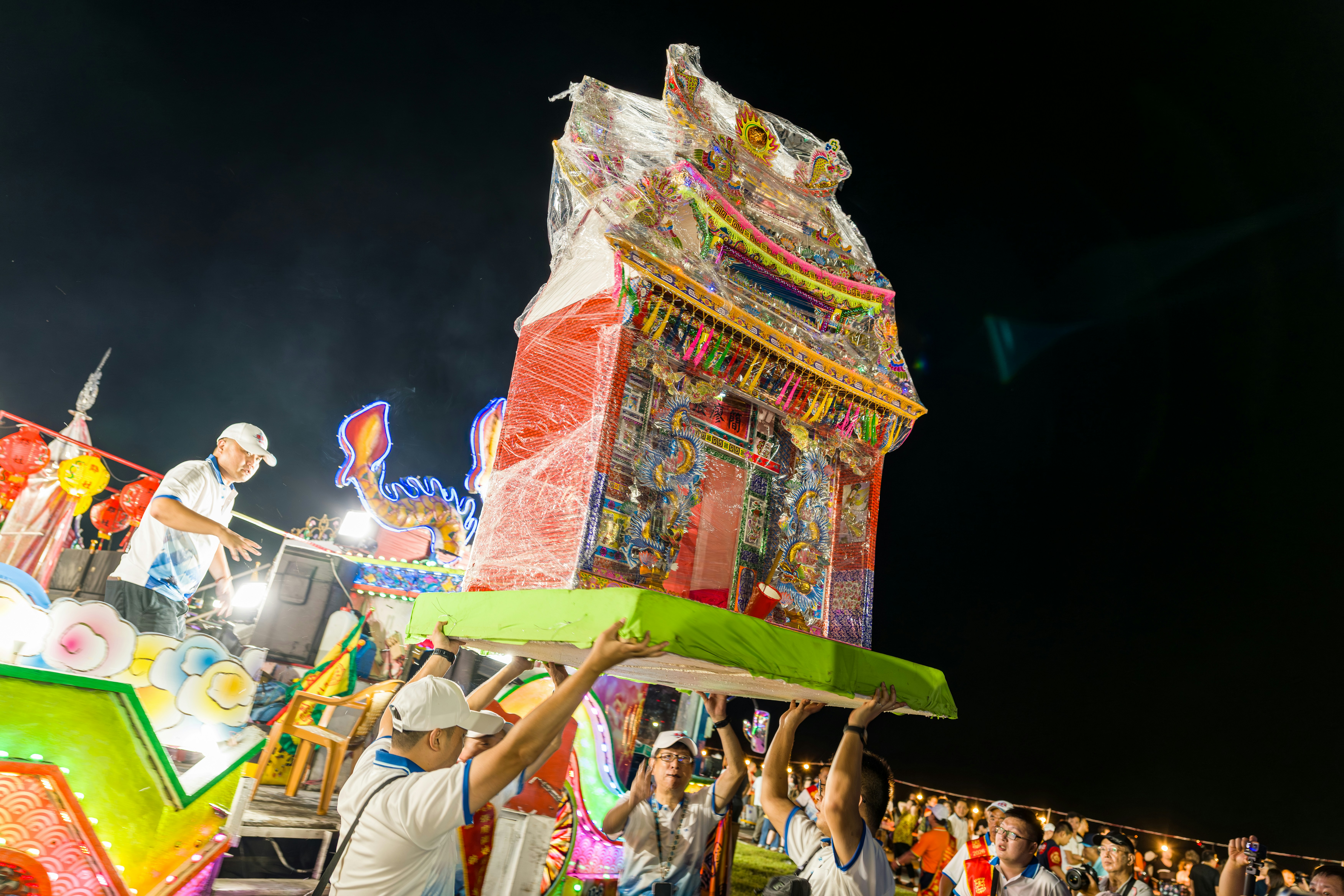 People in white shirts carrying a large ornate structure wrapped in plastic at night