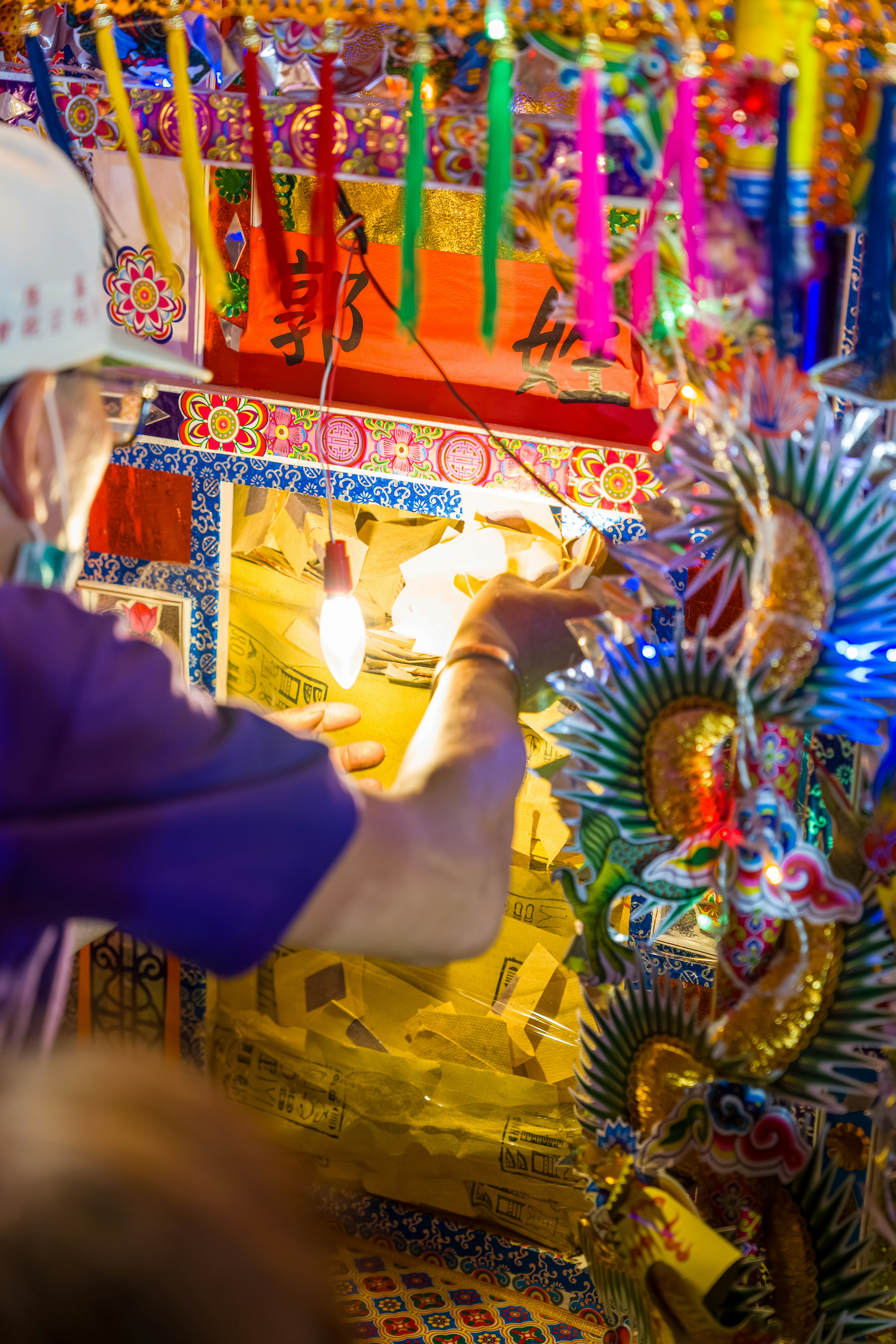 A person placing yellow paper into a brightly decorated traditional shrine with hanging tassels